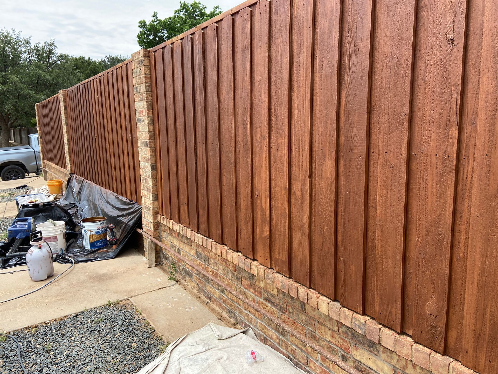 Wooden fence with brick base, stained brown. Construction supplies are visible nearby.