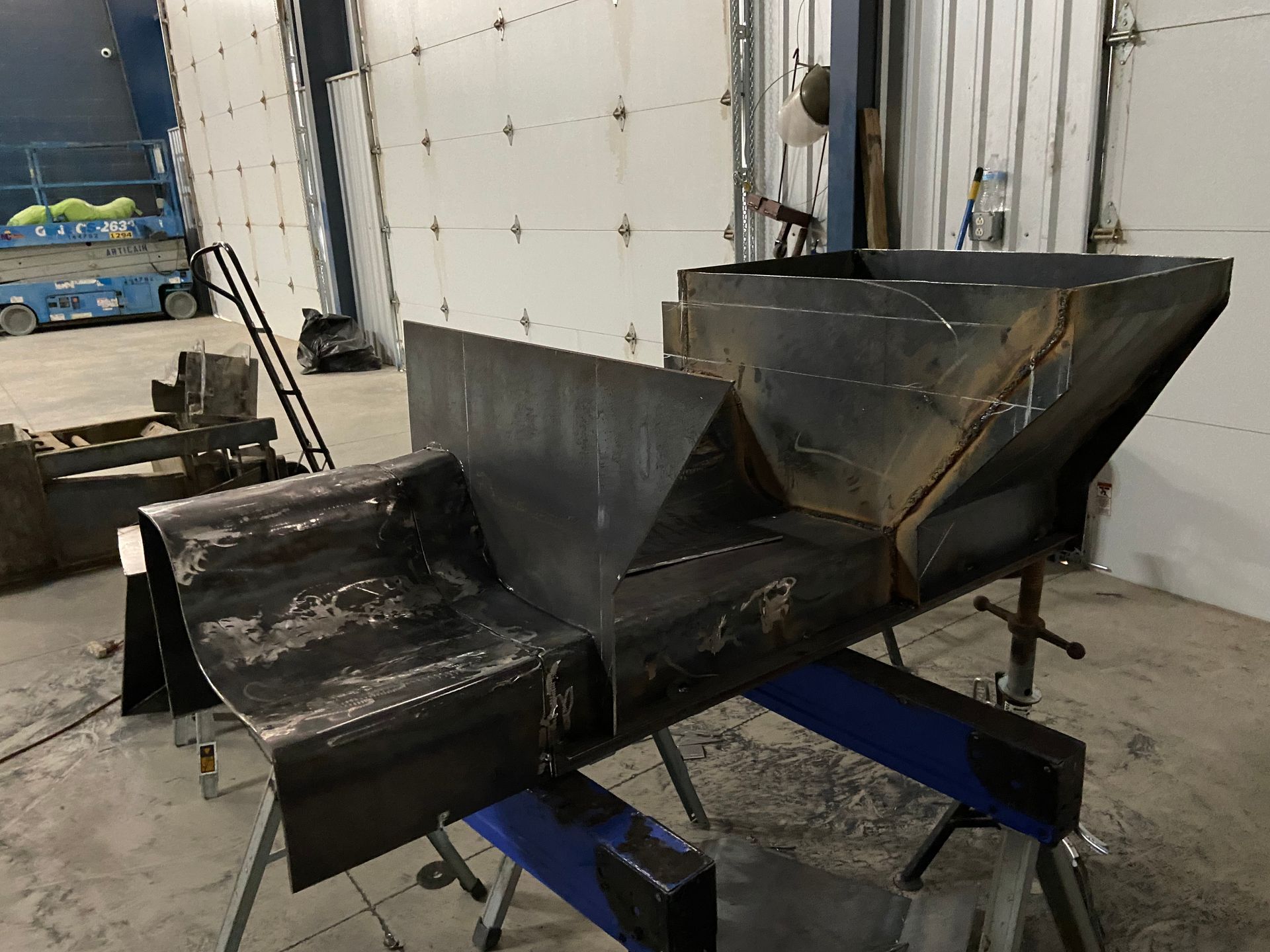 Welded steel hopper assembly on a workbench in a workshop.