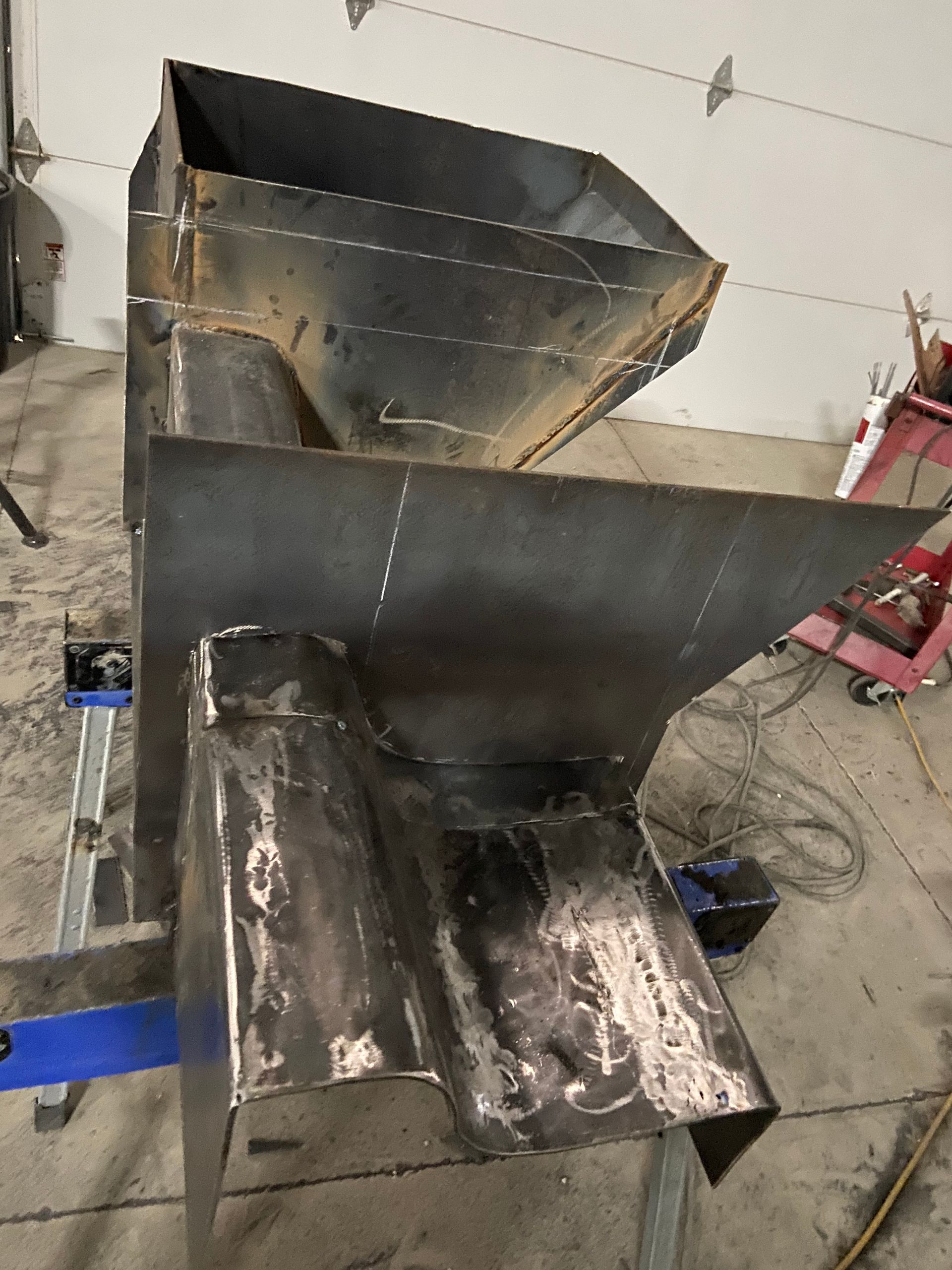 Large, fabricated metal hopper with welded seams, likely for industrial use, indoors.
