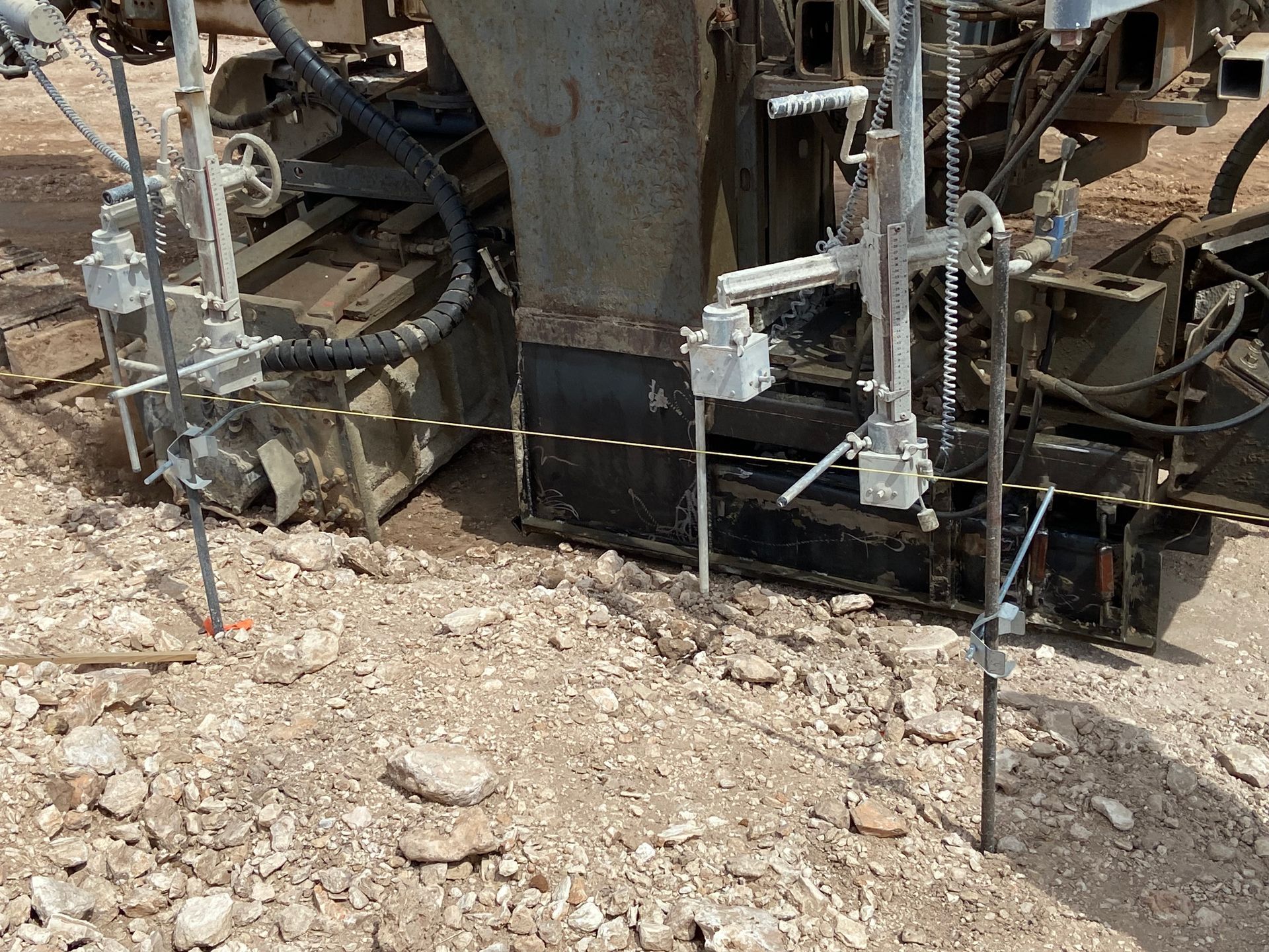 Pavement milling machine, with depth sensors, on a gravel surface.