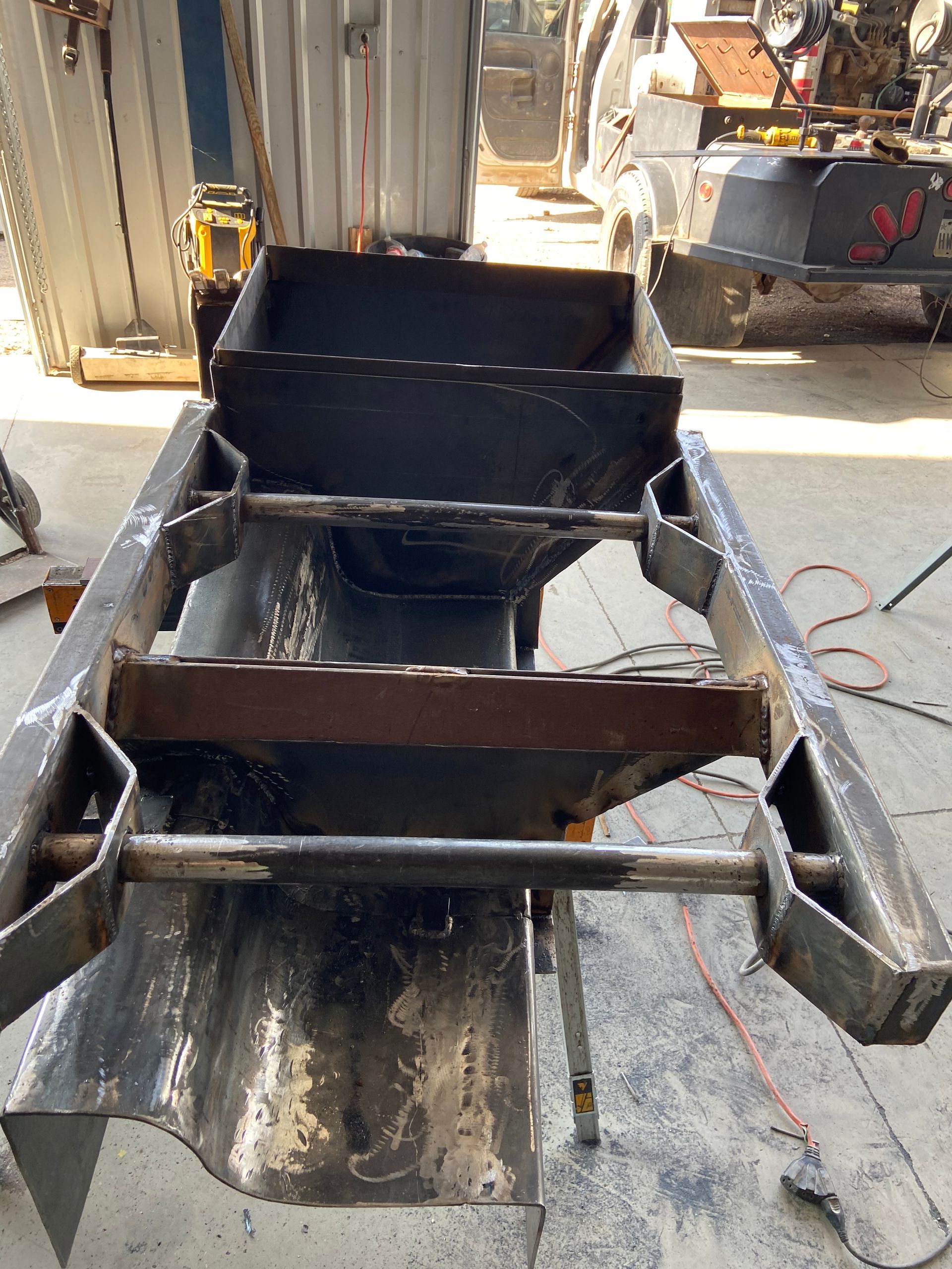Welded metal frame construction, outdoors, with a bucket and supporting structures visible.