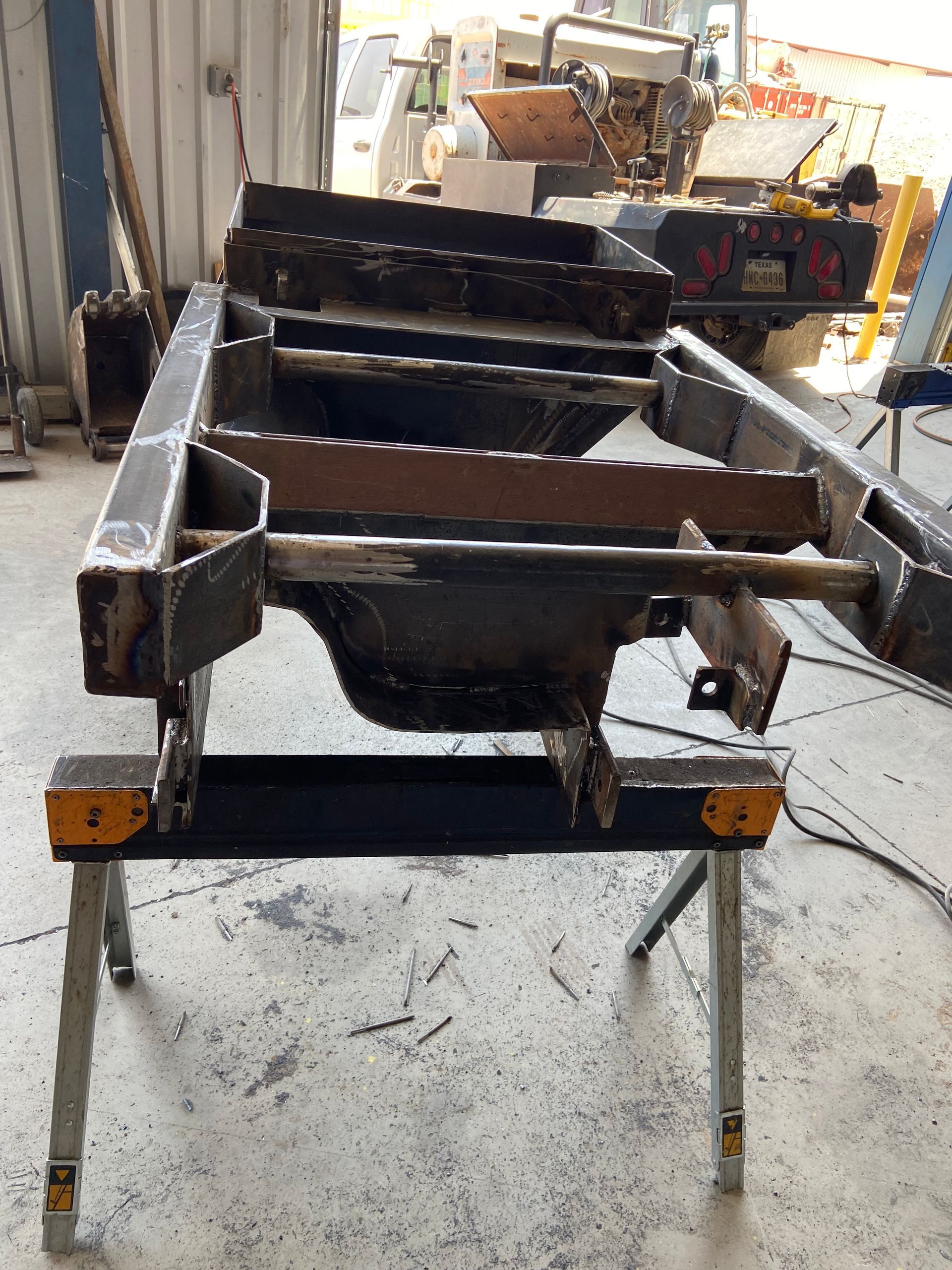 Metal chassis on sawhorse work stands in workshop.