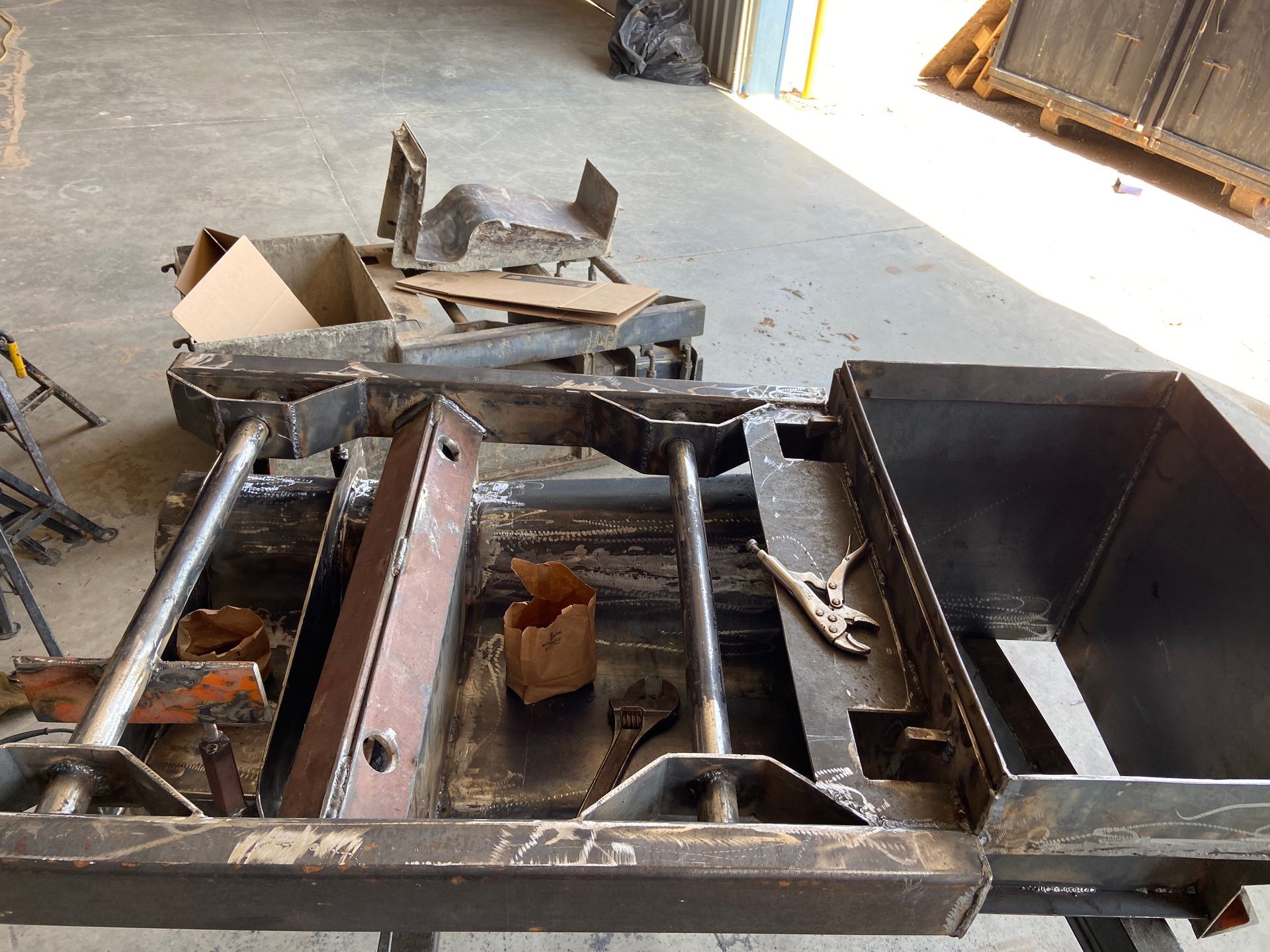 Metal fabrication in progress; welded frame with bins and supporting structures. Gray concrete floor.