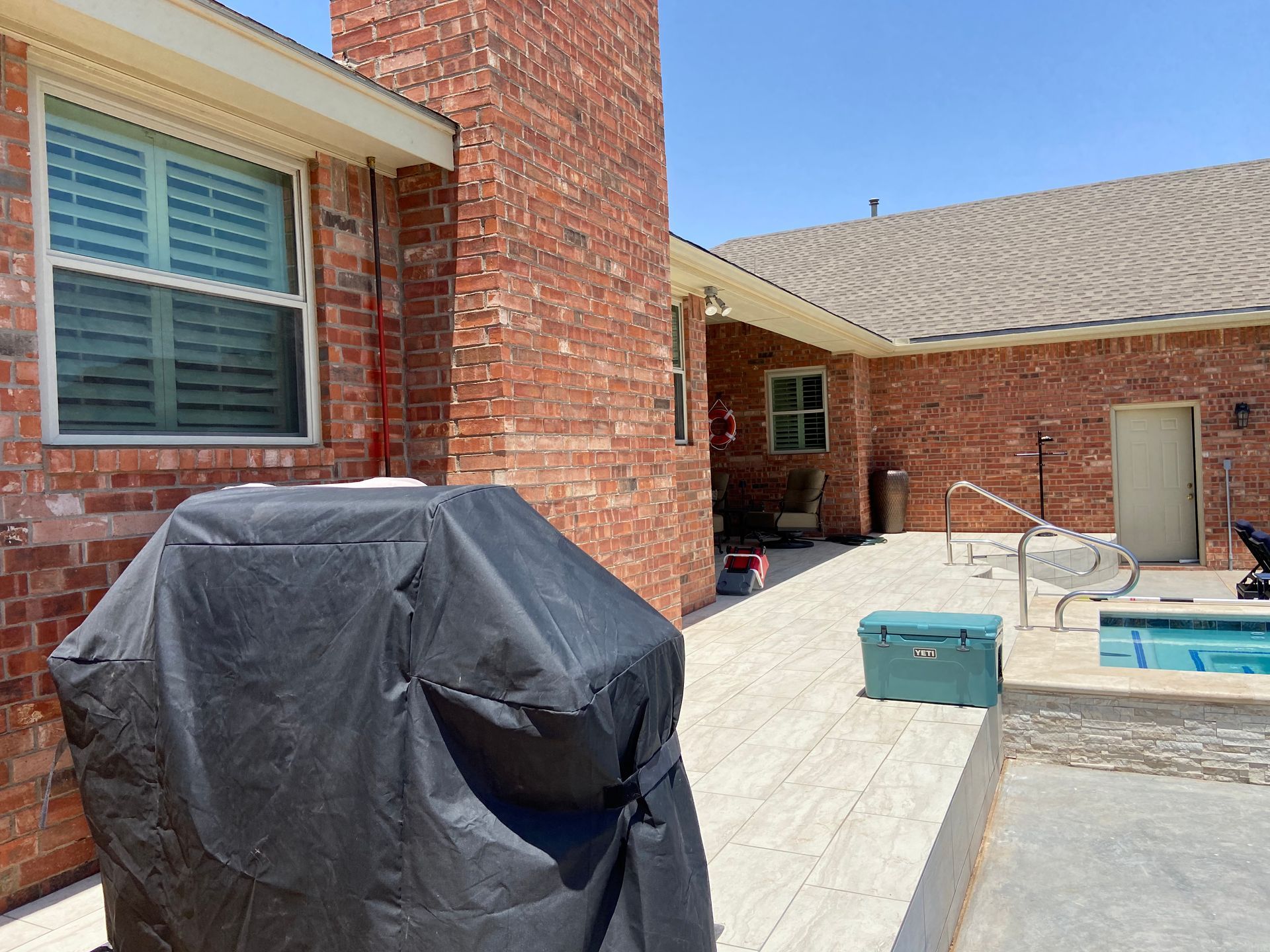 Backyard patio with brick chimney, grill cover, and a small pool.