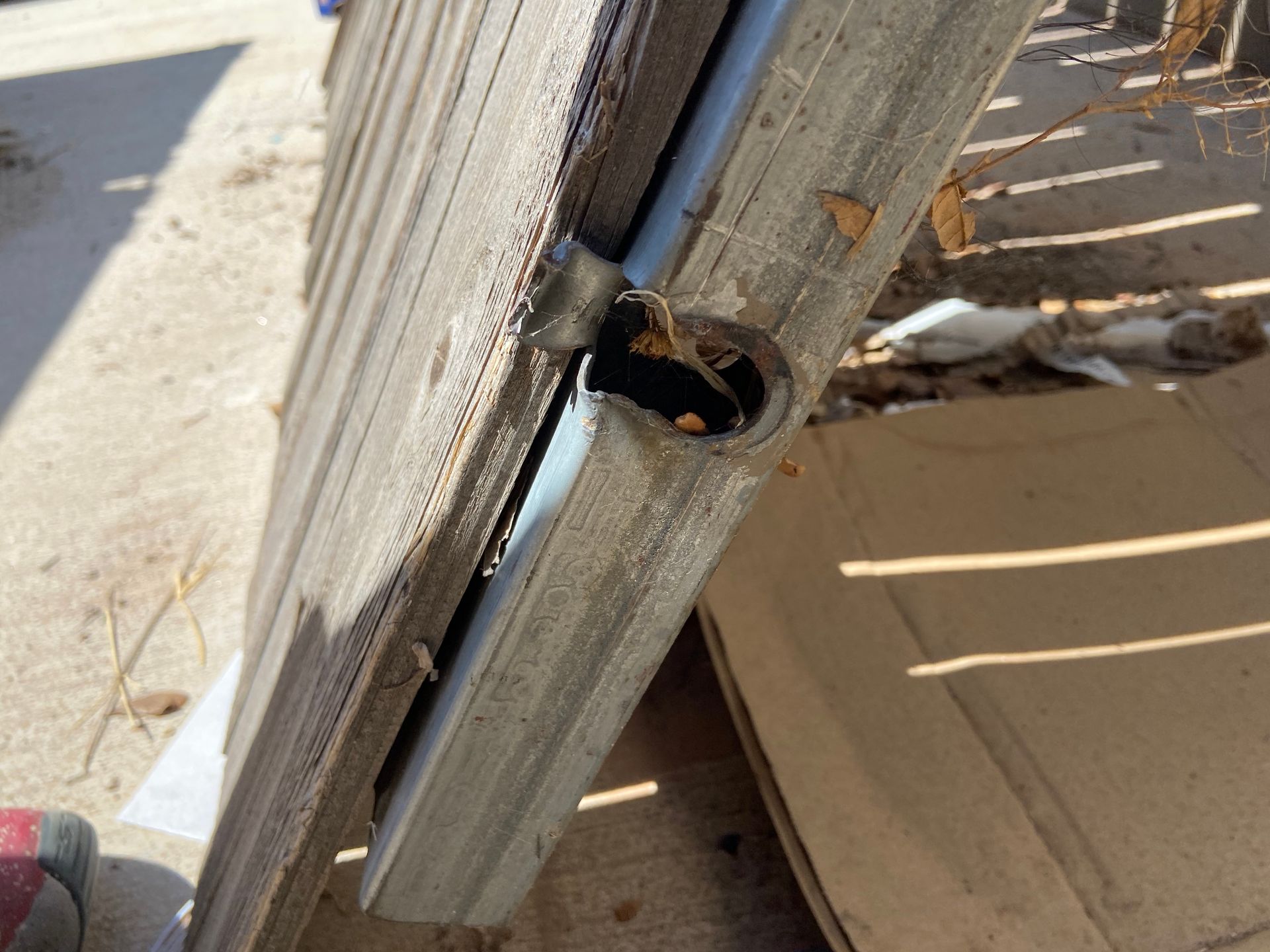 Wooden fence corner with a round hole, likely for a hinge, and a metal bracket.