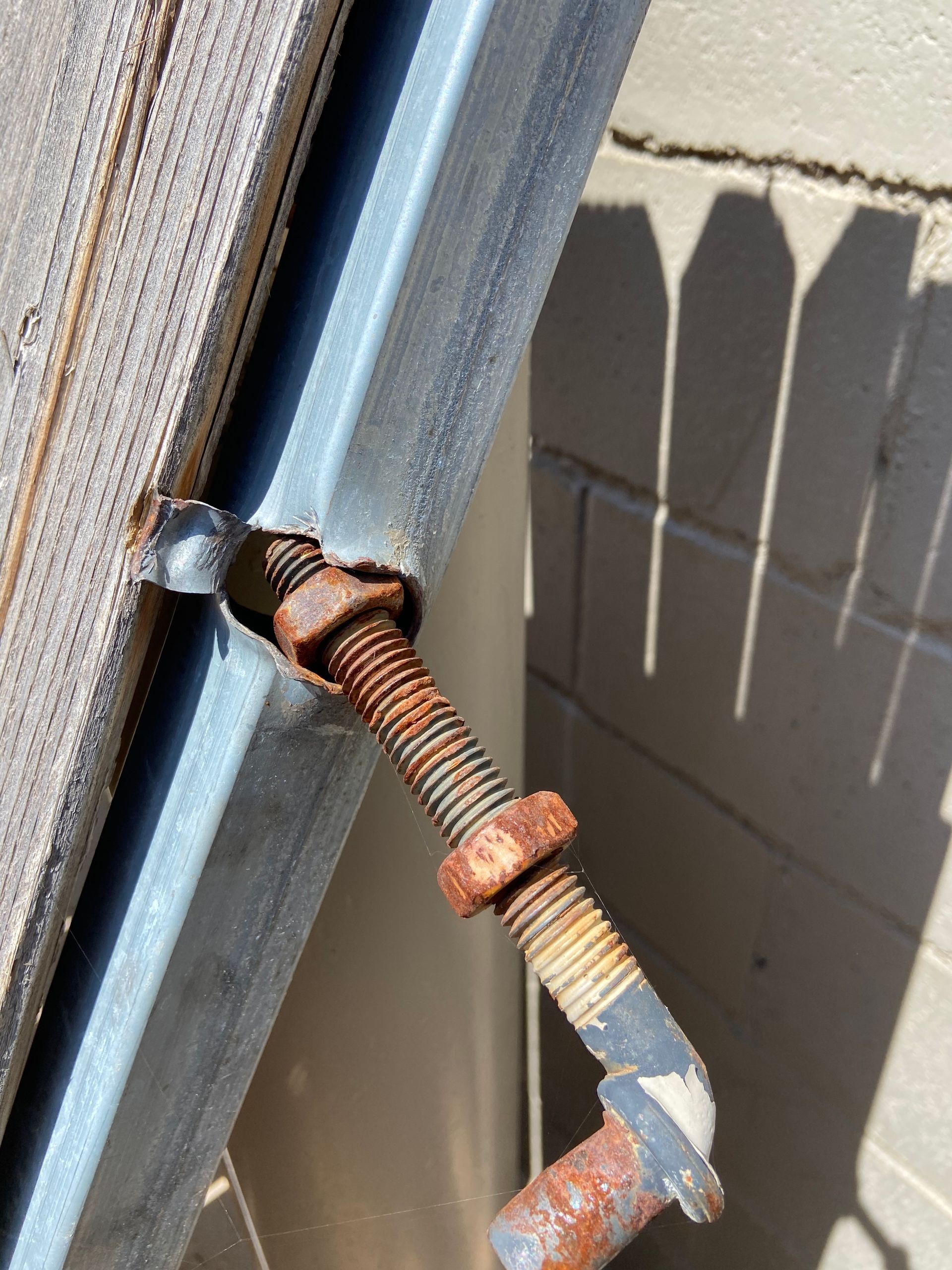 Rusty bolt and nut securing a solar panel frame, mounted on a building exterior.