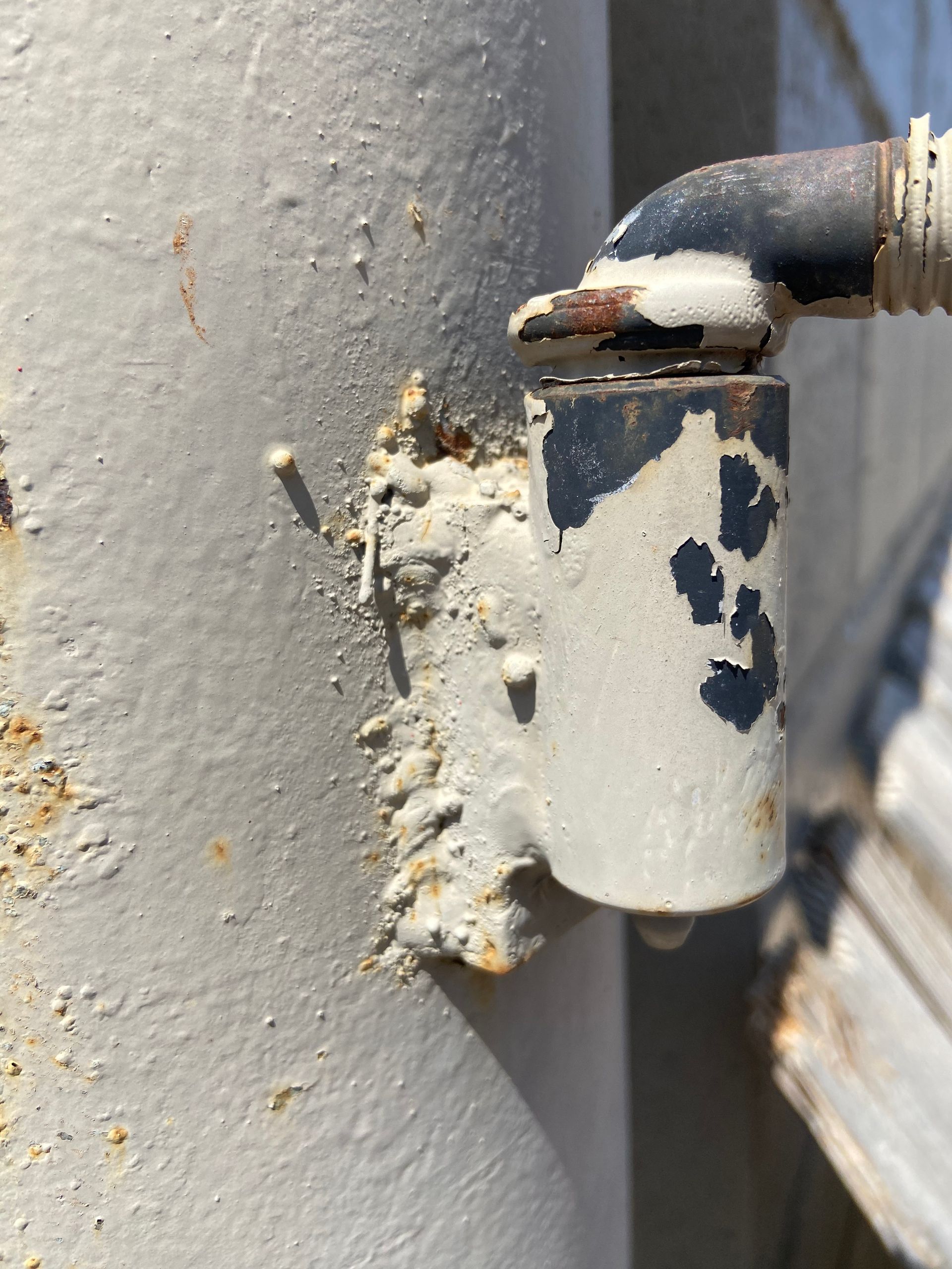 A metal pipe with a corroded hinge and a connecting pipe, all painted white and black.