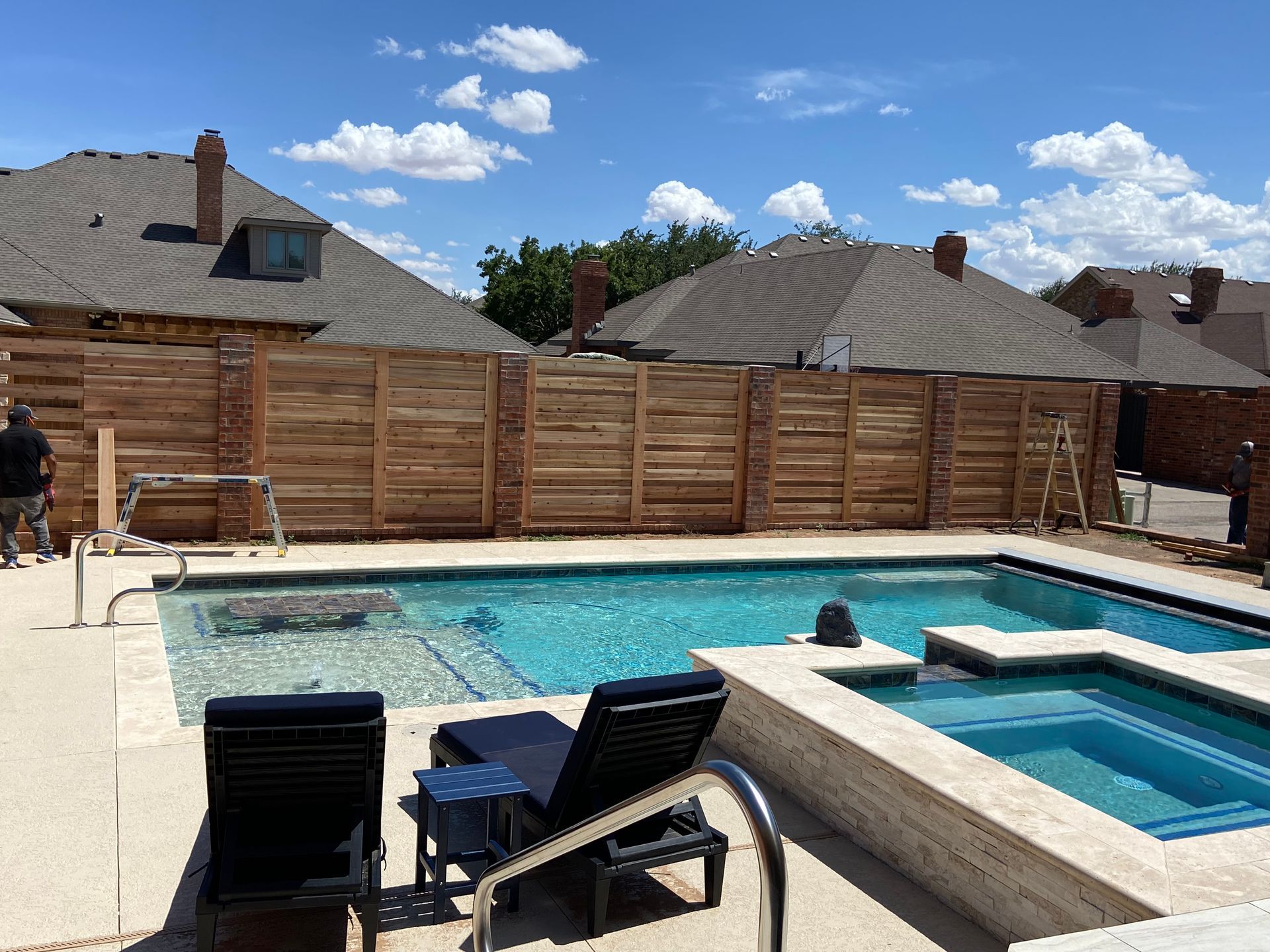Pool with lounge chairs and new wooden fence under a blue sky.