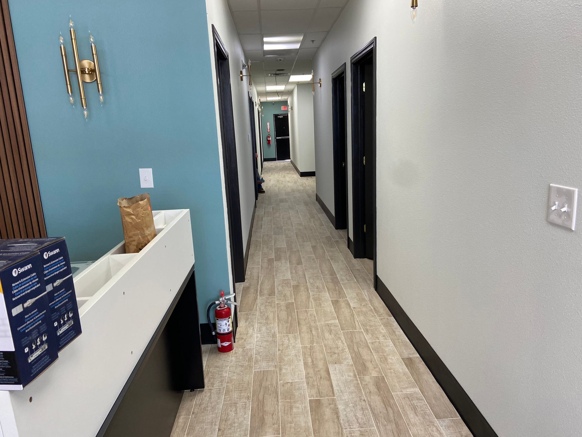 Hallway with doors, light wood-look flooring, teal accent wall with gold decor, and white reception desk.