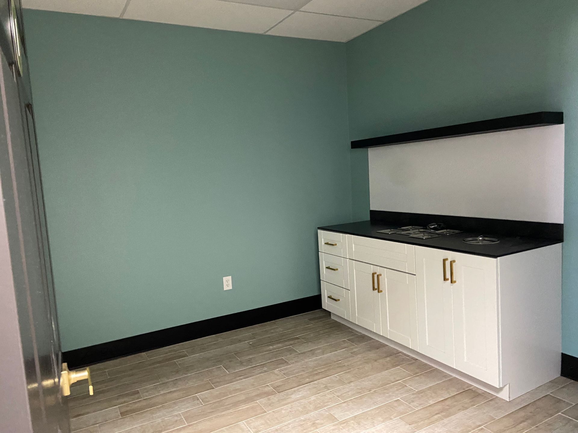 Empty room with white cabinets, black countertop, blue-green wall, and wood-look flooring.