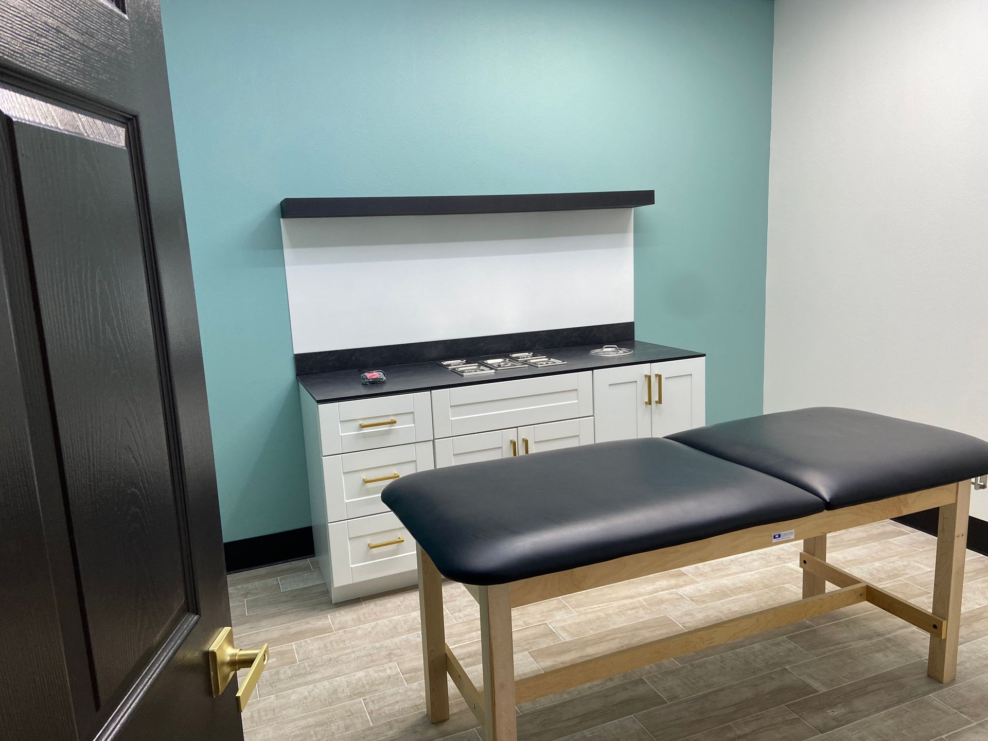 Examination room with a white cabinet, medical table, and teal wall.
