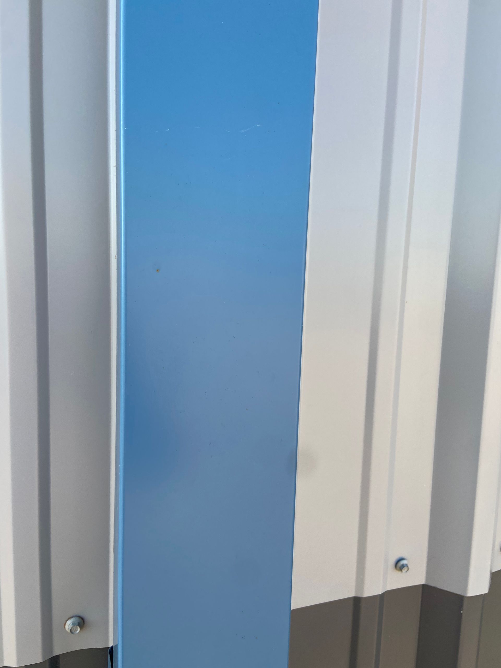 Vertical blue metal beam against a corrugated metal wall.