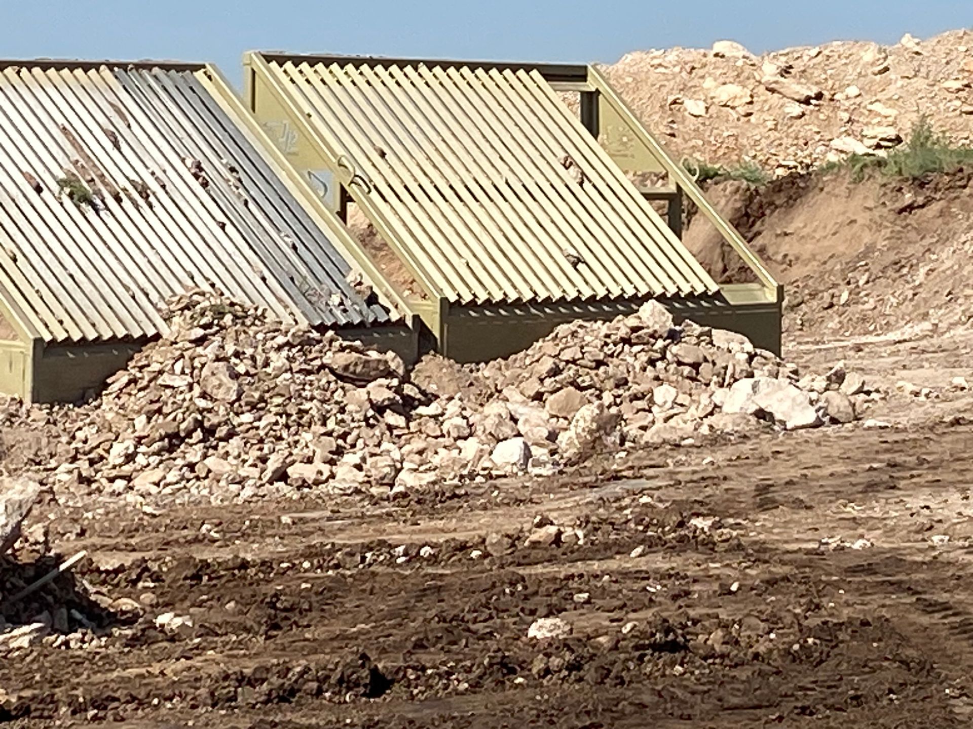 Two rectangular, corrugated metal structures with dirt piles in a construction site.