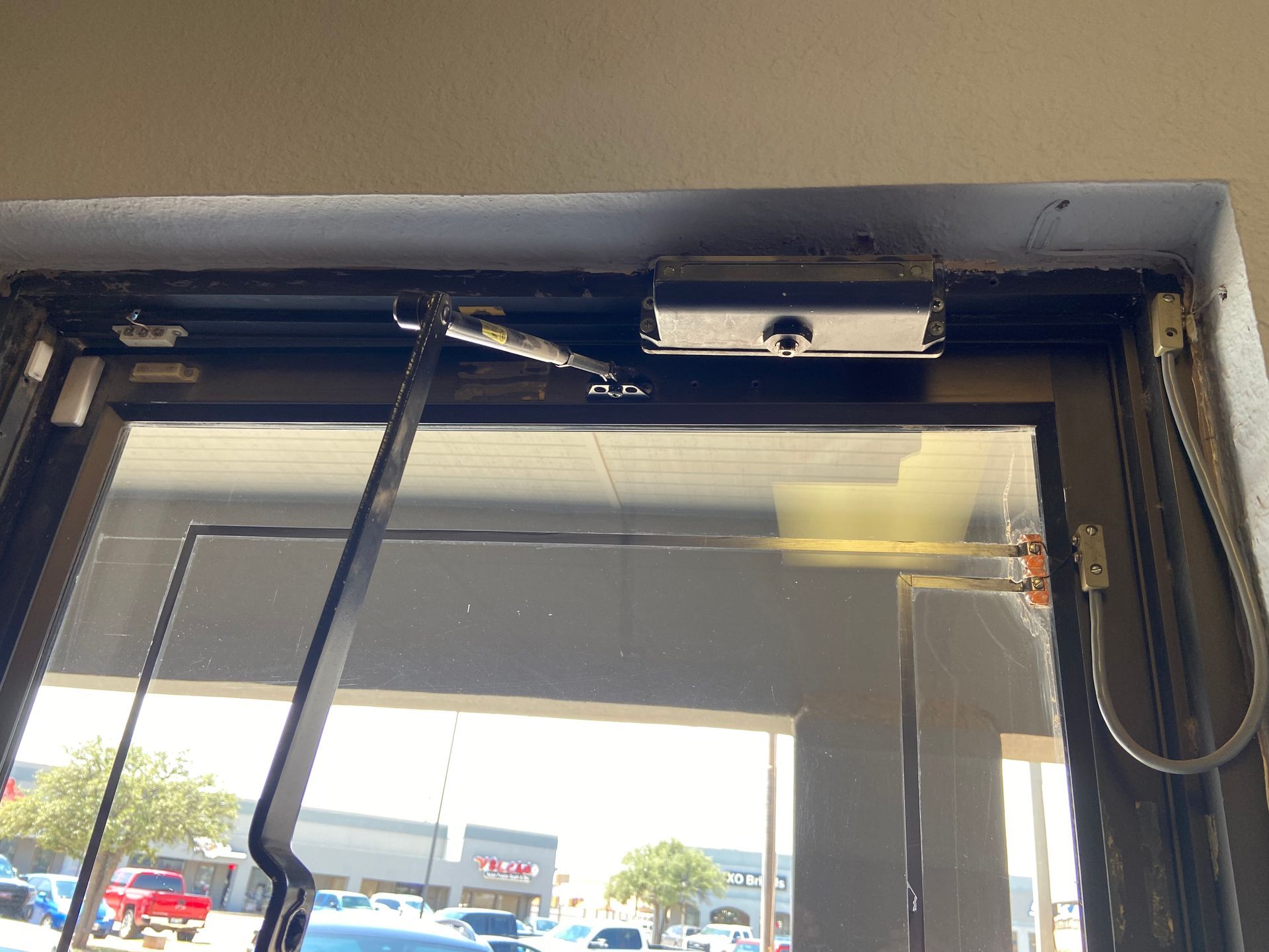 Door with automatic closer and long arm, viewed from inside, looking out to a street scene.