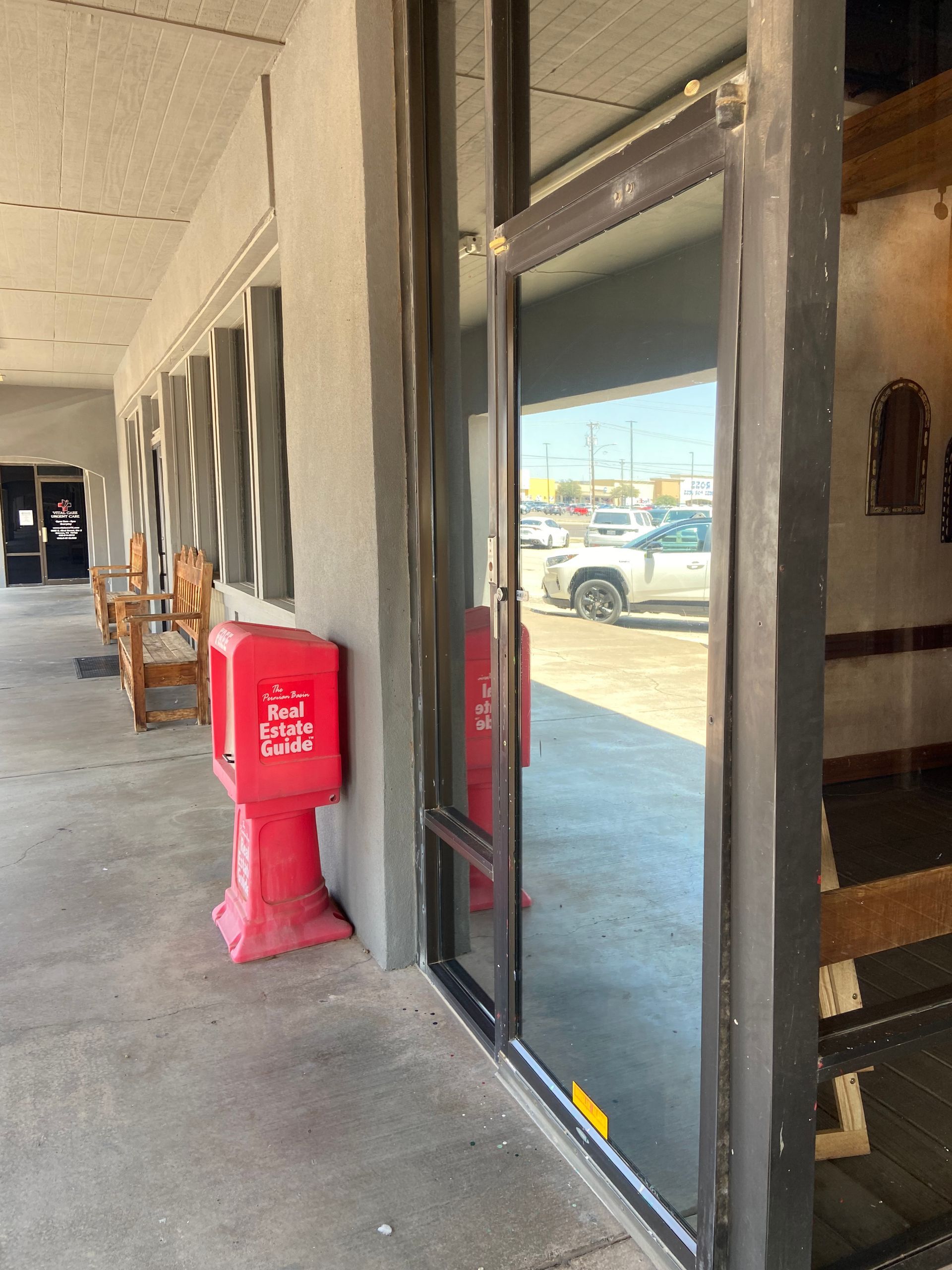 Exterior of a building with a glass door, a red donation box, and parked vehicles visible in the reflection.