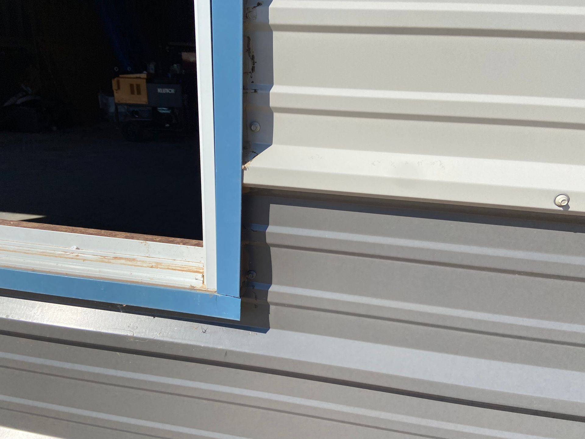 Open window frame with blue trim on a gray corrugated metal building.