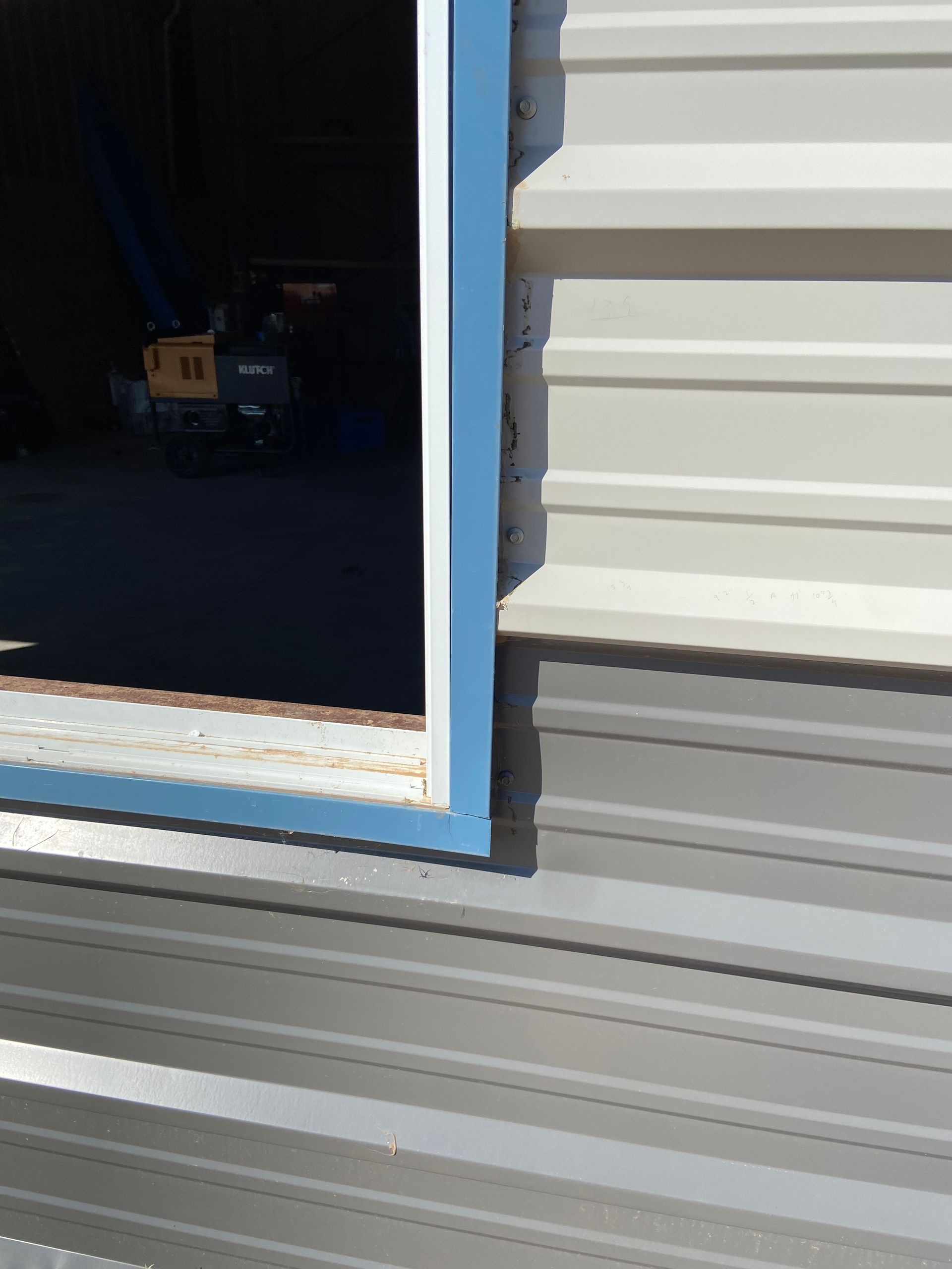 Metal building door frame with blue trim, partially open, revealing equipment inside.
