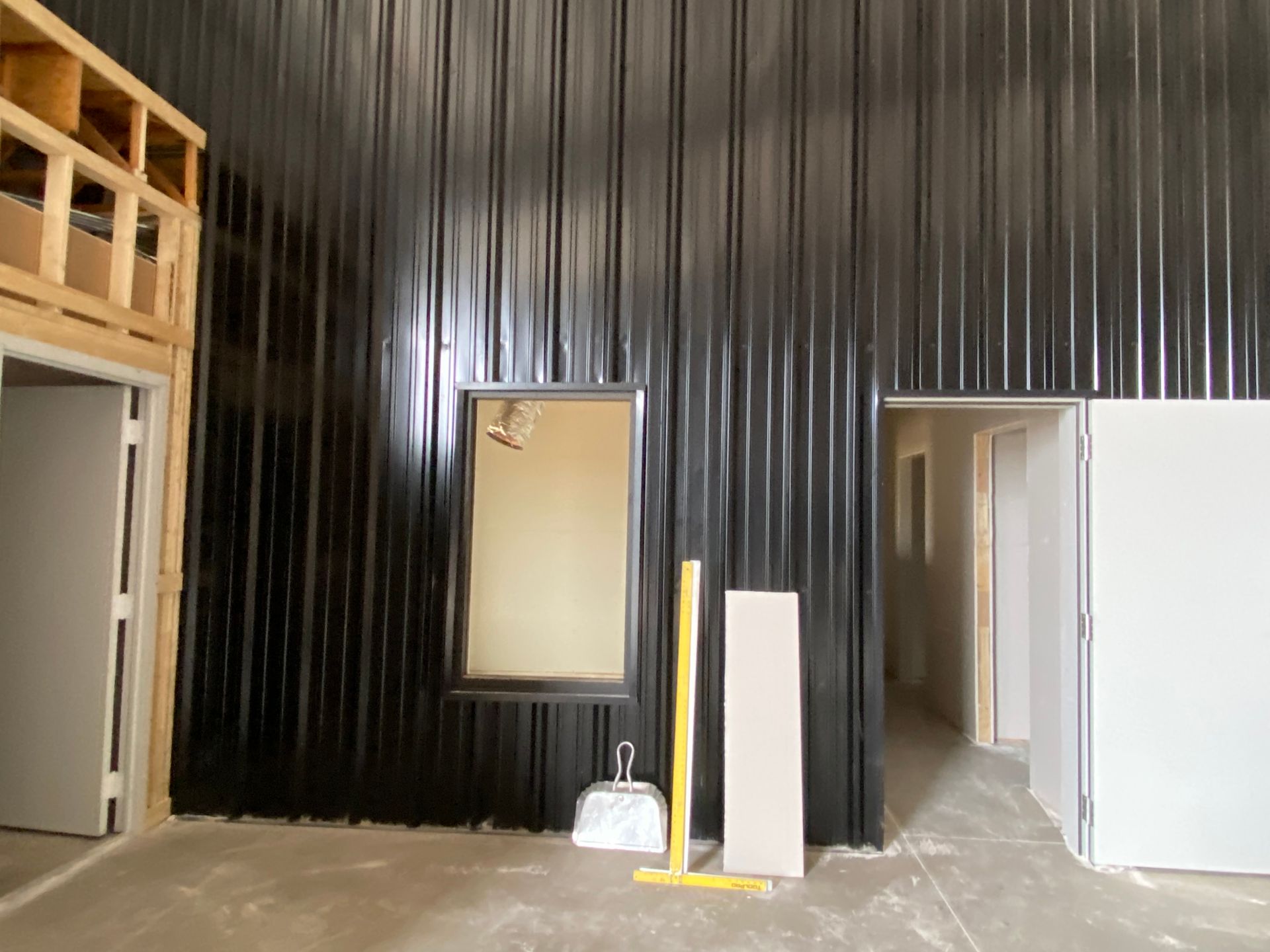 Interior with black corrugated metal wall, small window, and open doorways. Construction debris visible.