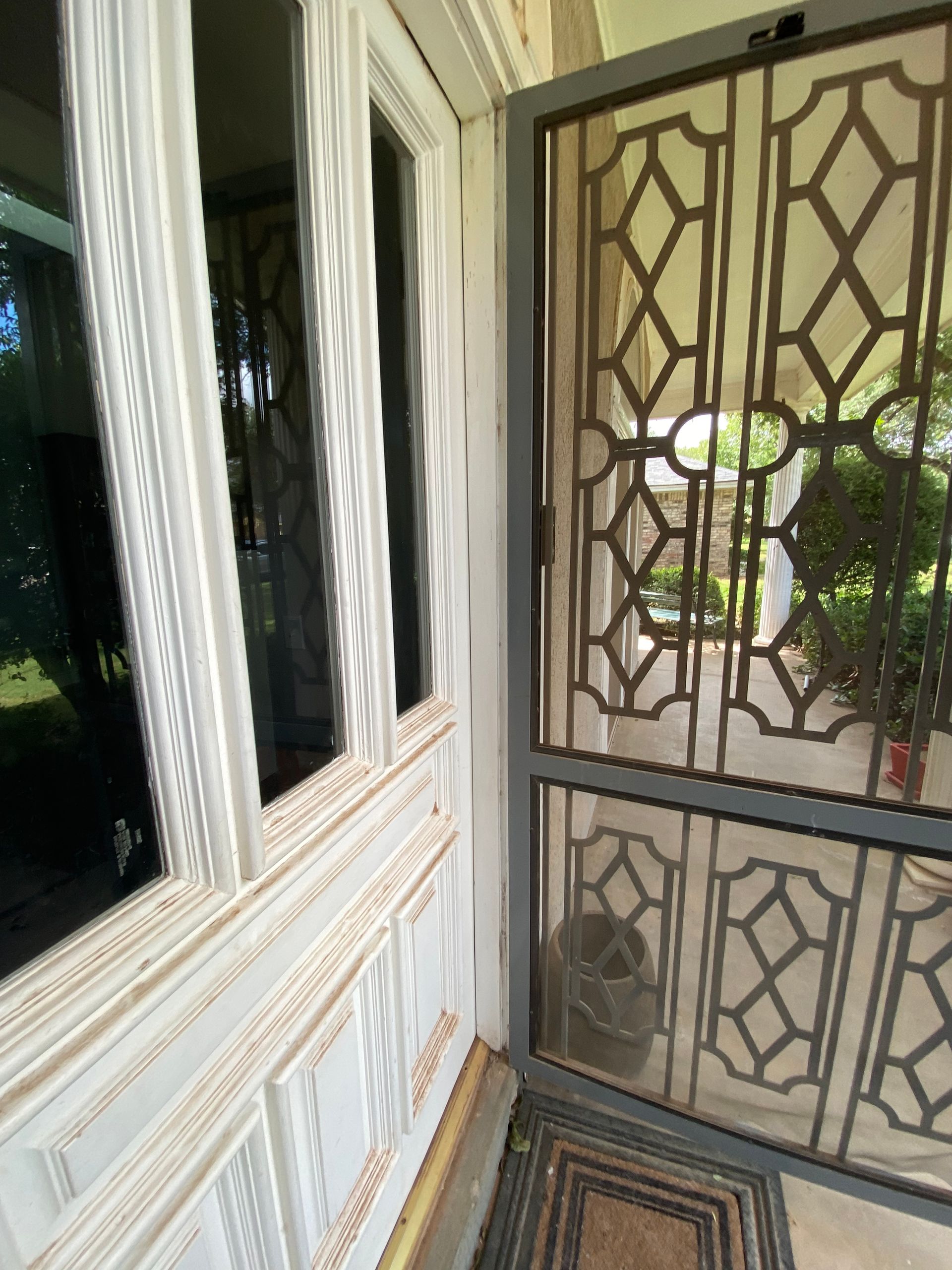 White-framed door with decorative metal screen; interior view of a porch with window and doormat.