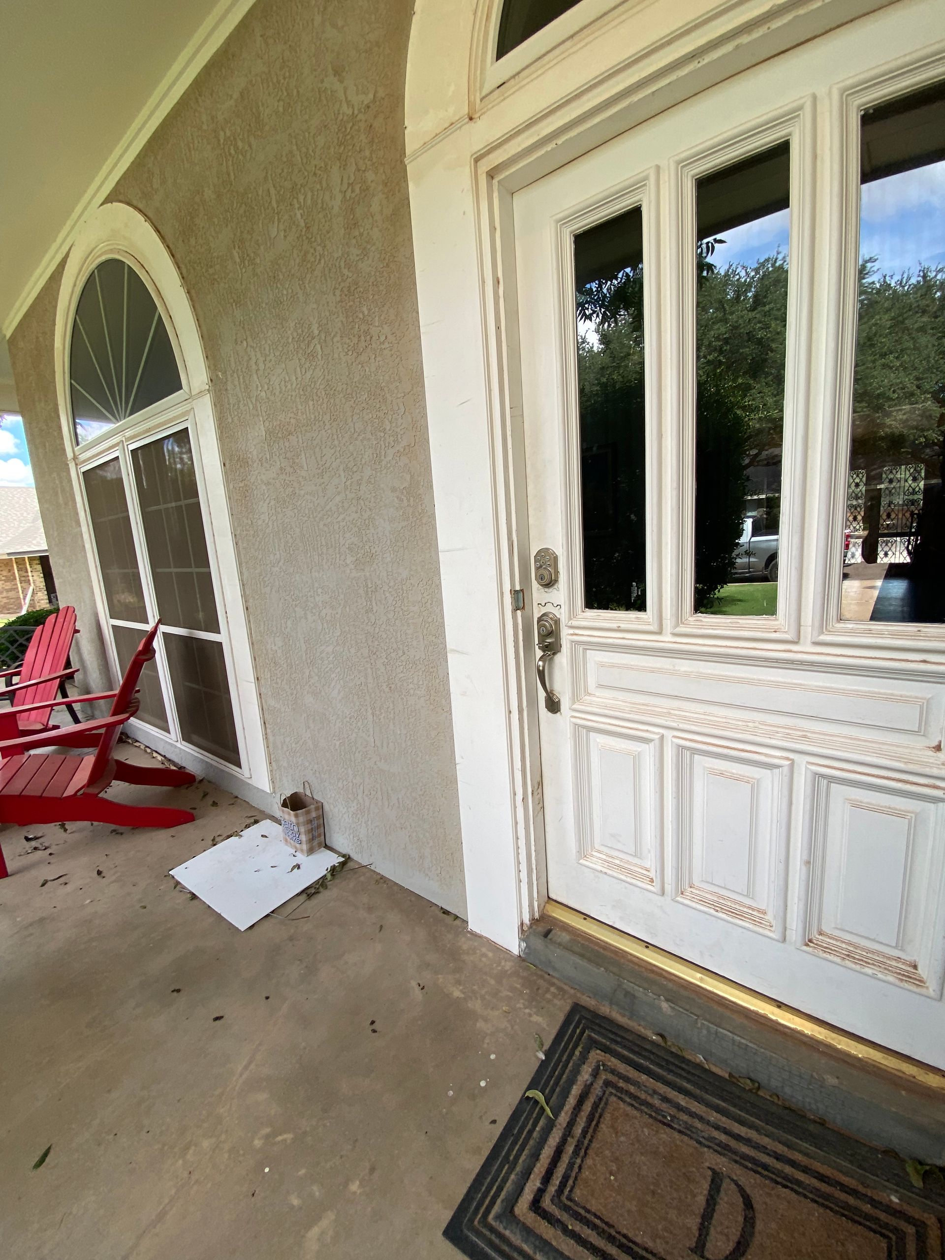 White front door with glass panels and a welcome mat on a porch with stucco wall.