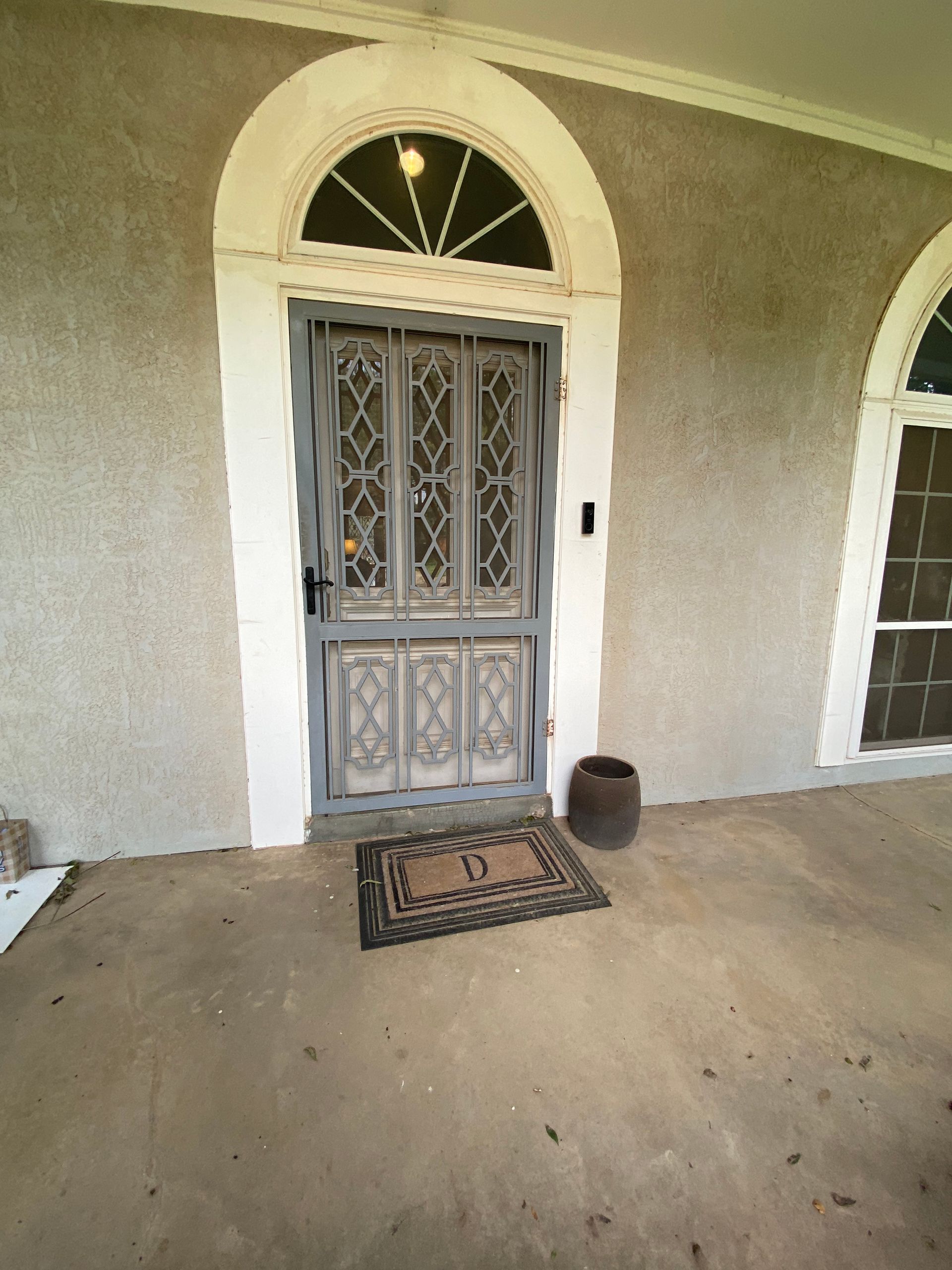 Gray front door with arched top and ornate metal security screen. Welcome mat on porch.