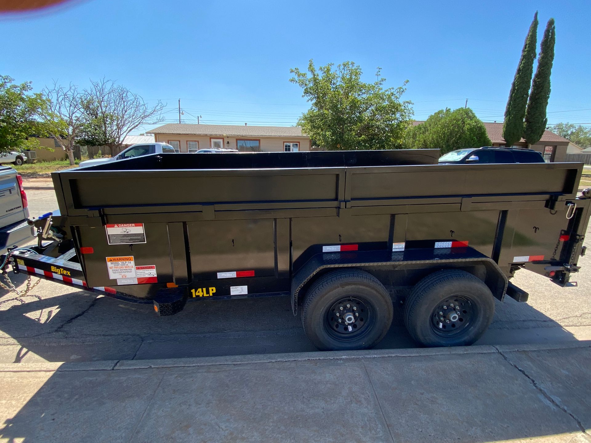 Black dump trailer parked on pavement, sunny day.