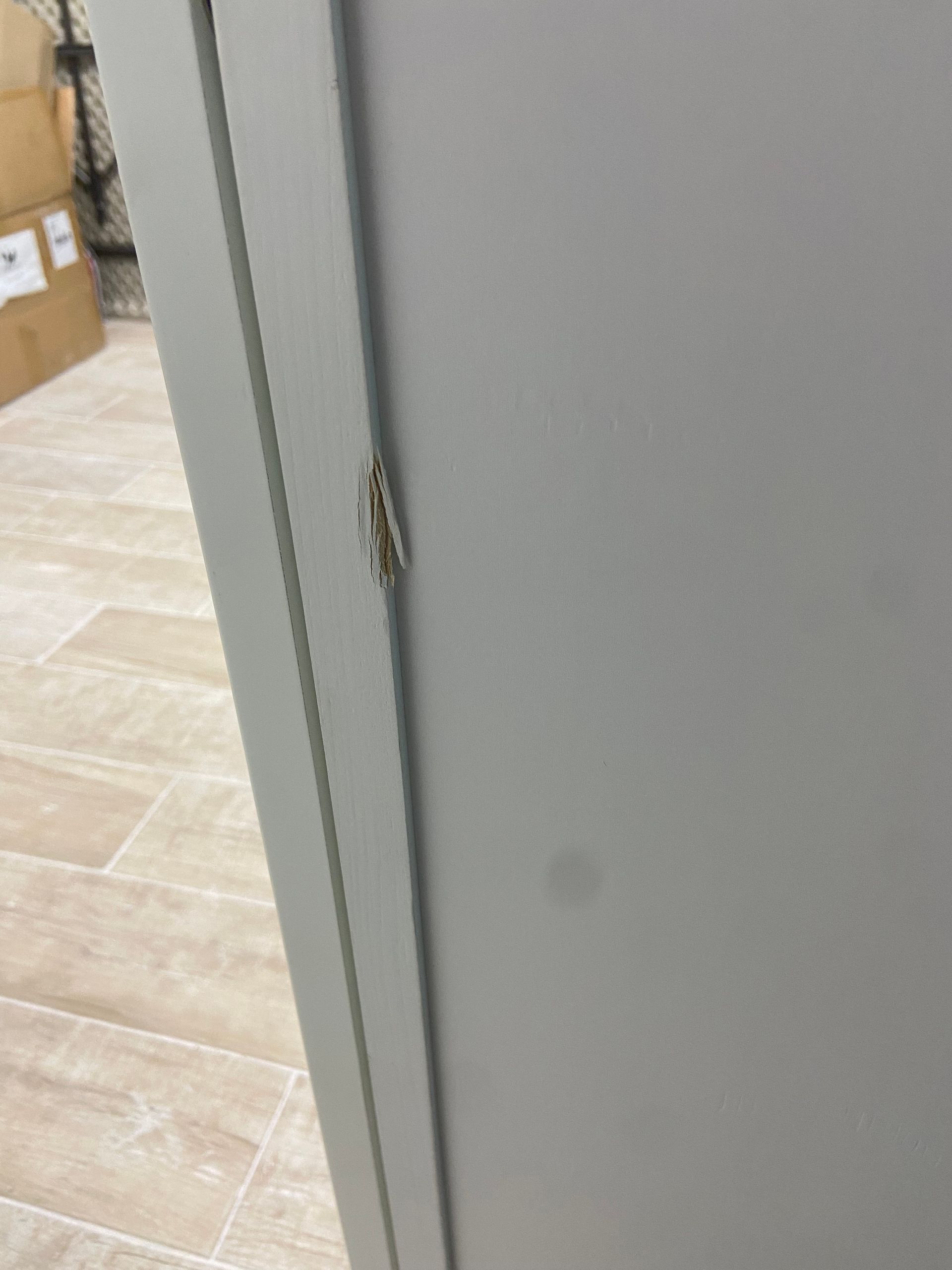 A close-up of a gray cabinet door with a silver metal hinge.