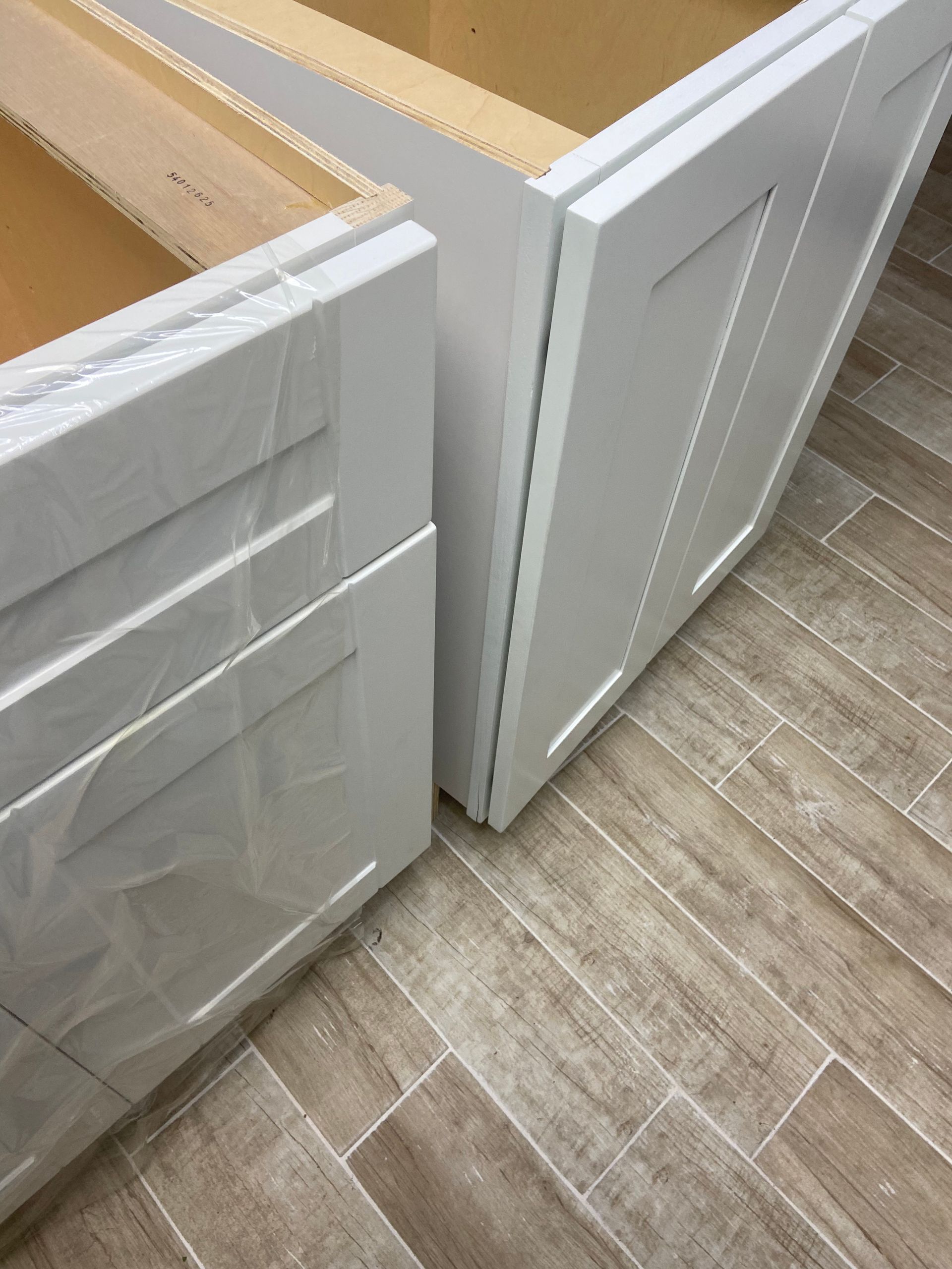 White kitchen cabinets, partially assembled, on a tile floor.