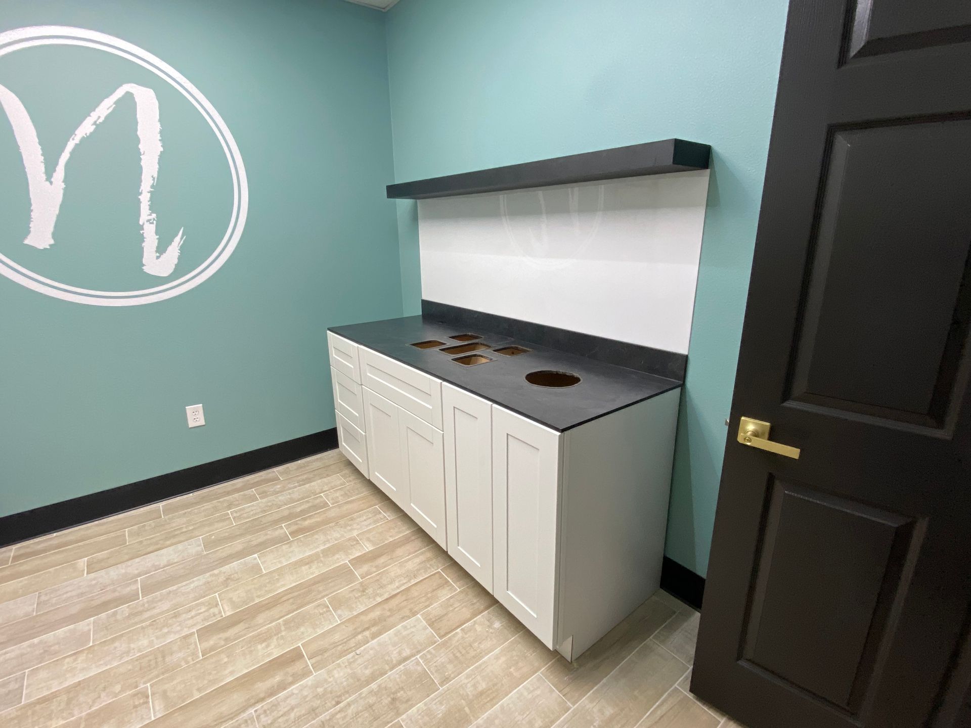 White cabinet with black countertop in a room with a light blue wall. Circular logo on the wall.