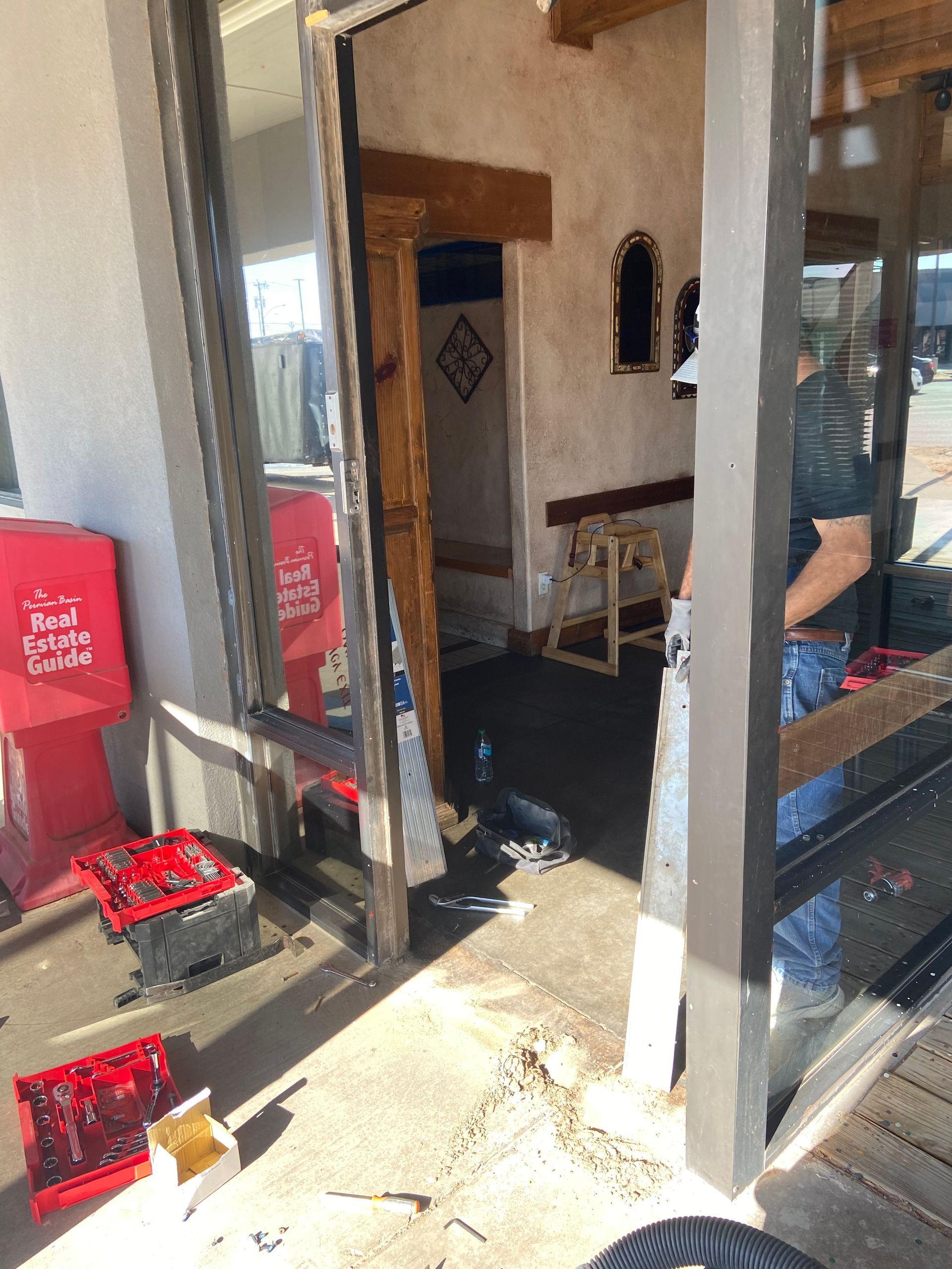 Shattered glass storefront, debris on ground, person standing nearby. Inside space with wooden accents.