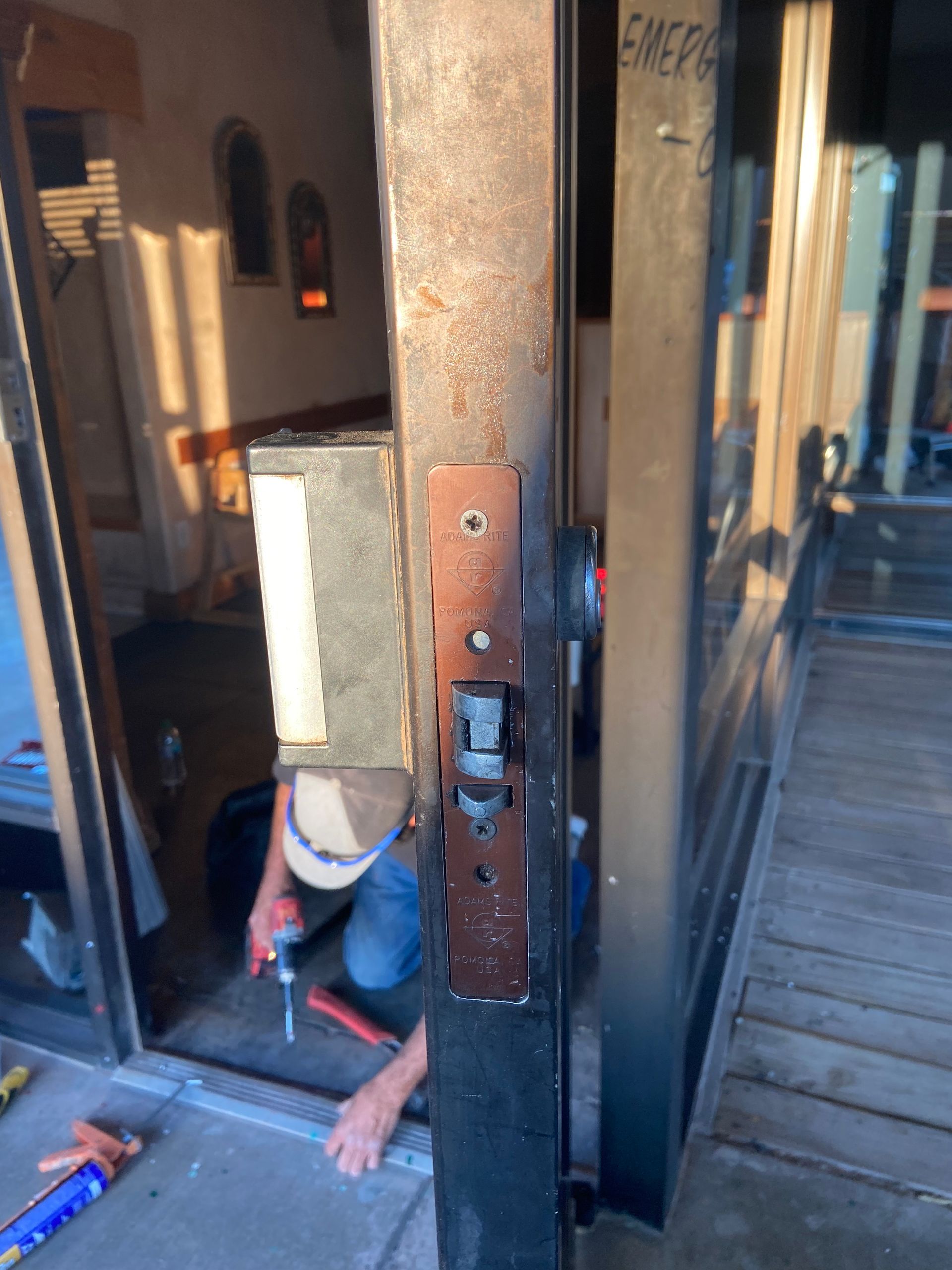 Person repairing a sliding glass door. They are kneeling, using a power drill. Door frame shows rust.