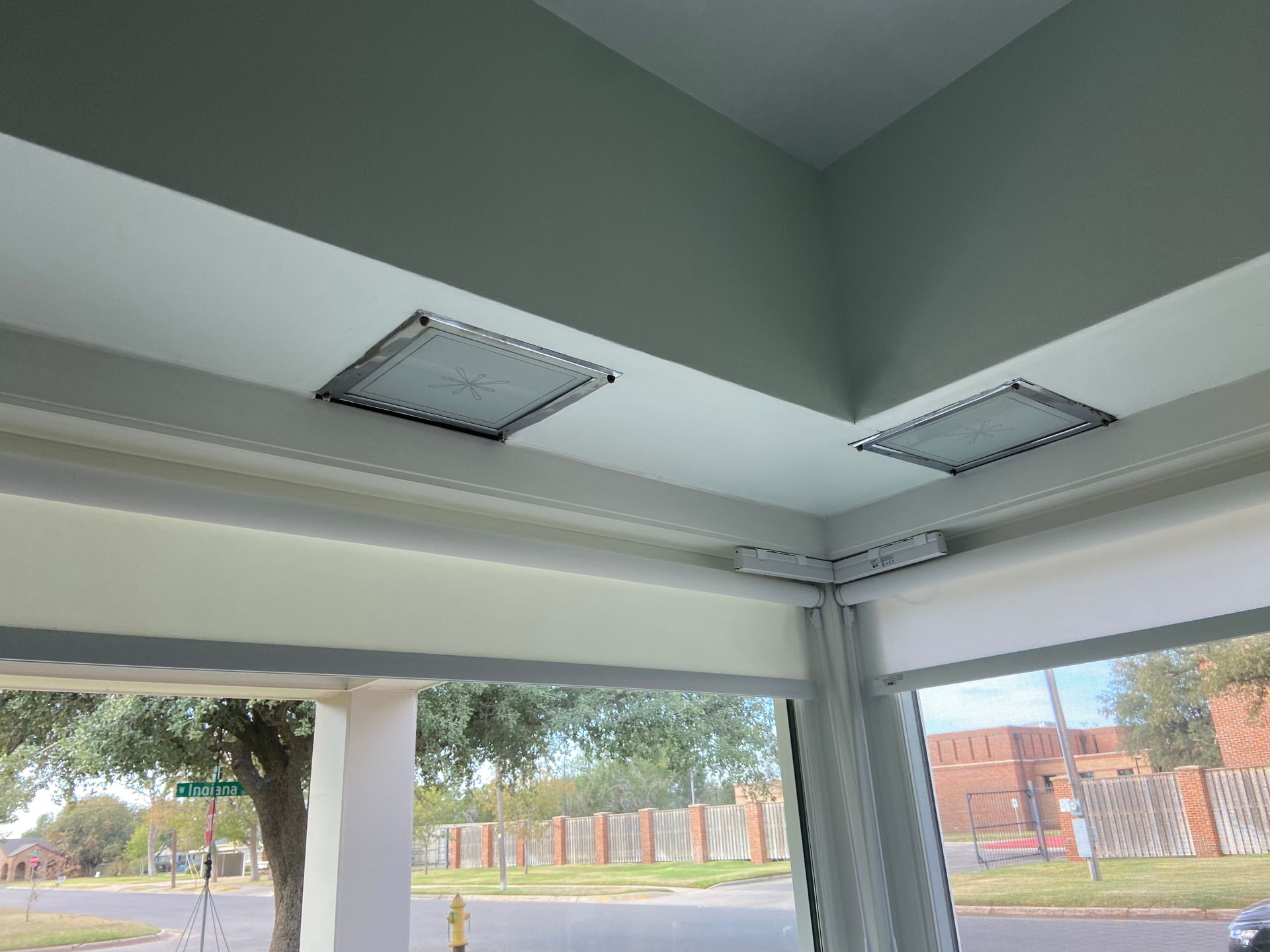 Corner room with two square ceiling lights above large windows overlooking a street.