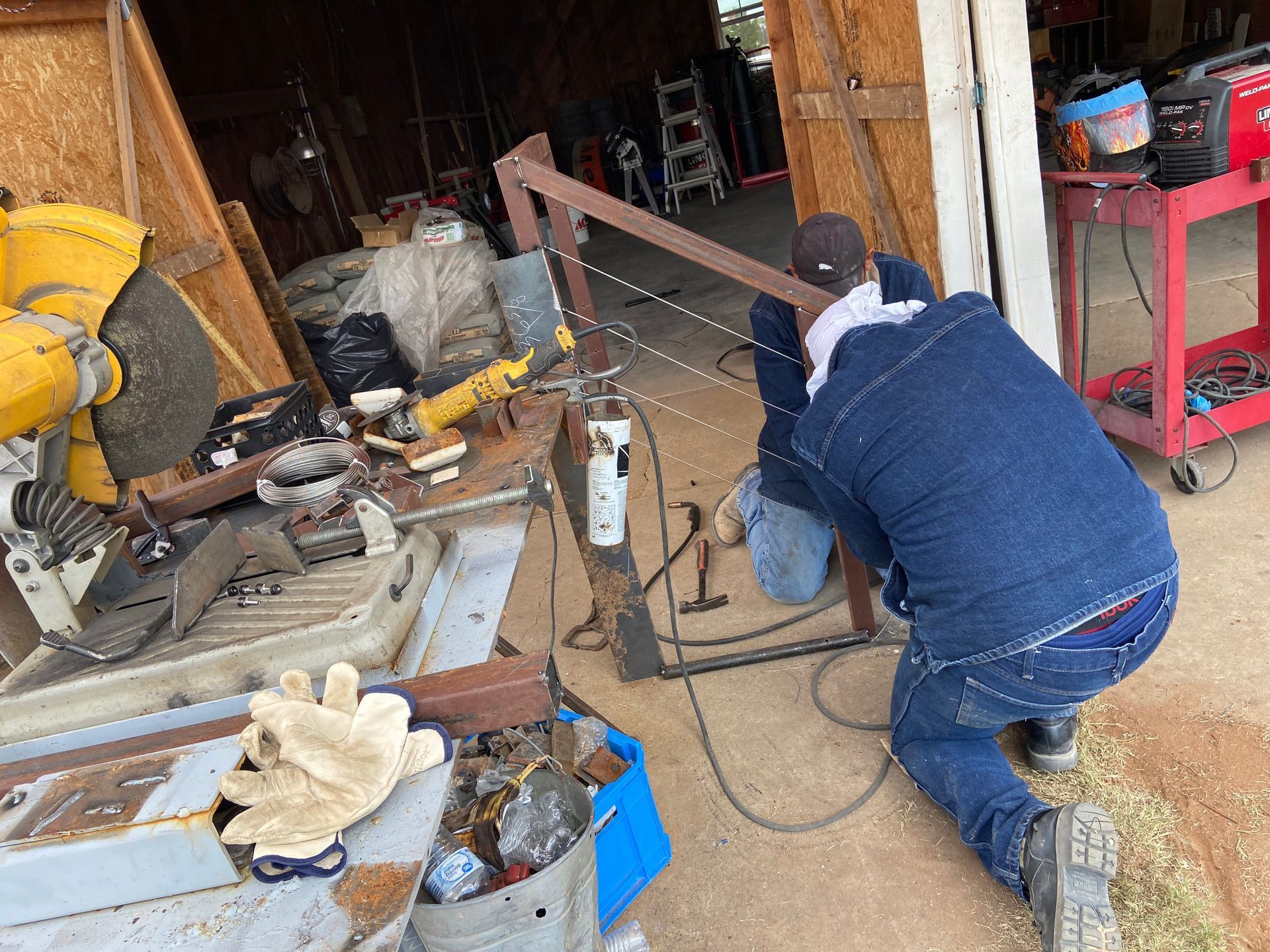 Person in denim jacket welding metal frame outdoors near tools.
