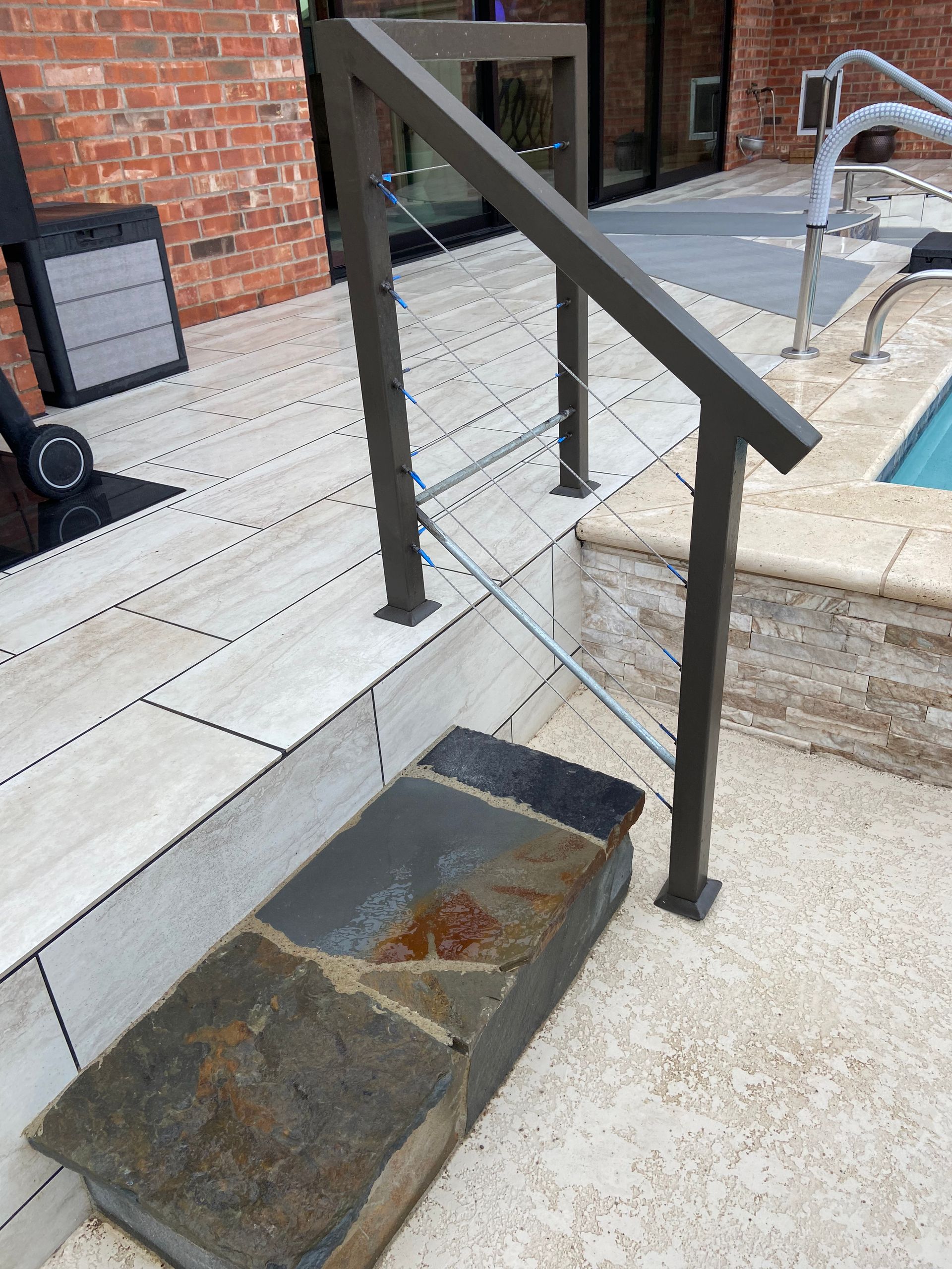Outdoor stairway with a metal handrail and cable infill next to a swimming pool.