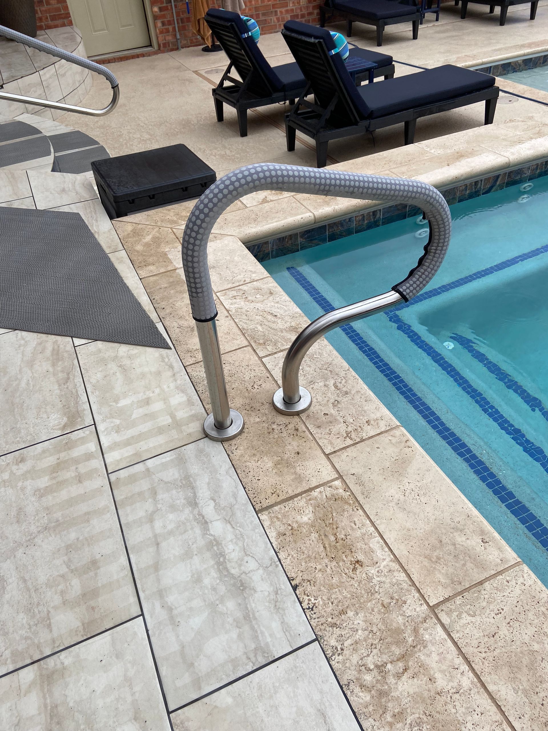 Pool with a handrail, lounge chairs, and tiled deck.