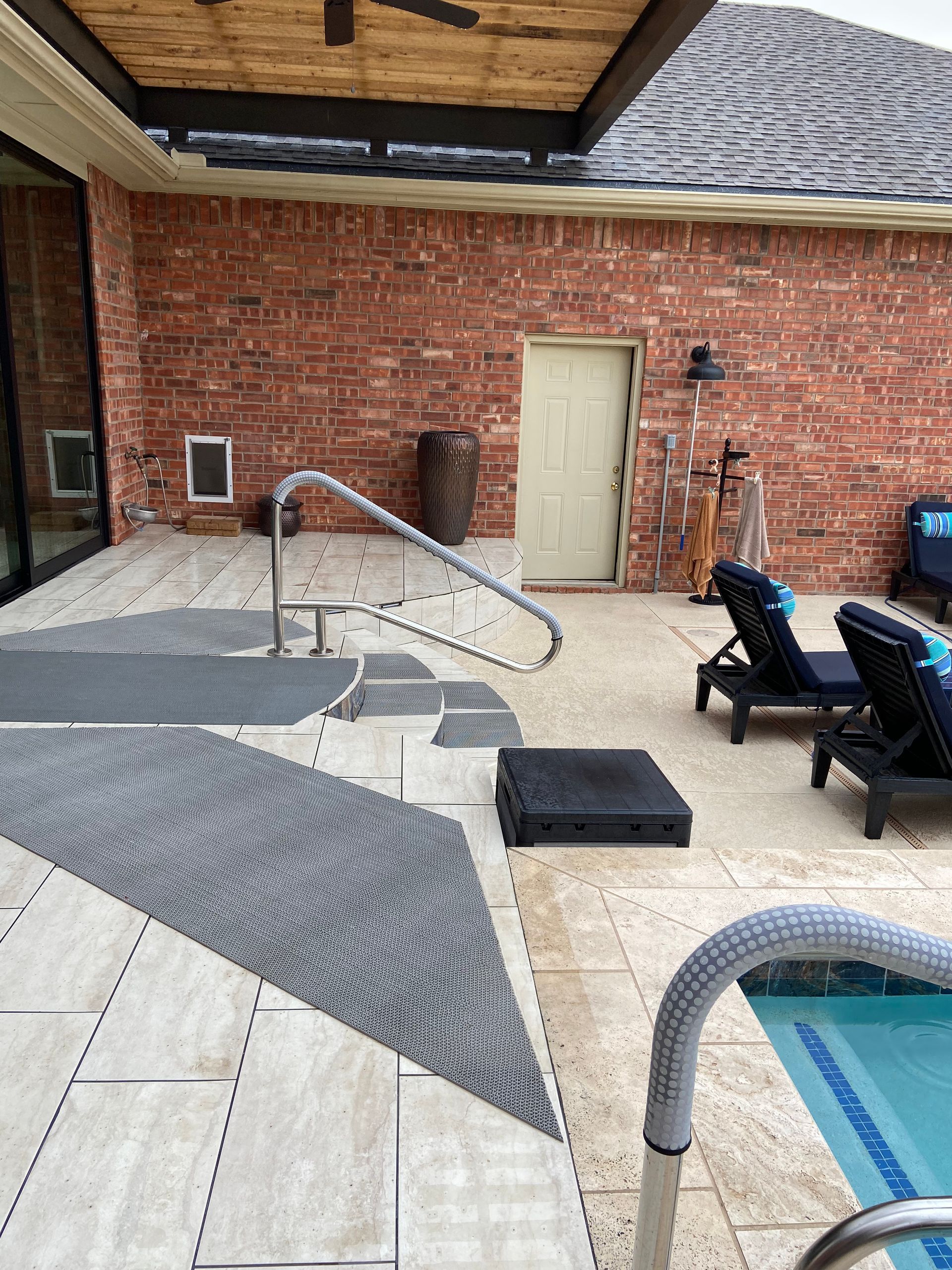 Backyard with pool, brick wall, lounge chairs, and a handrail for pool access.