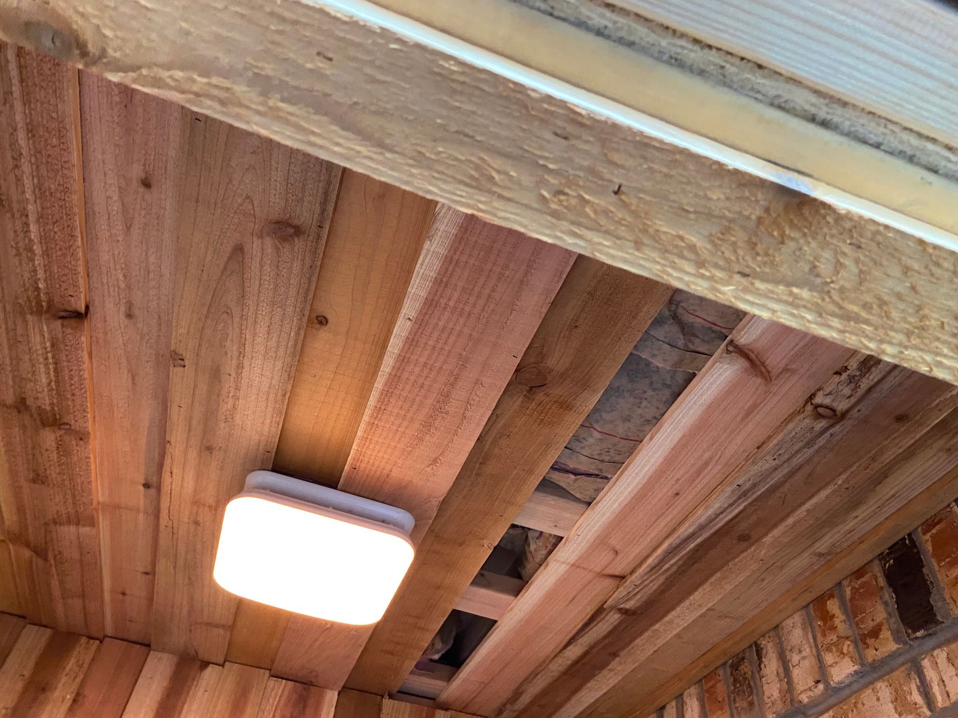 Wooden ceiling with a lit square light. Boards vary in color and direction.