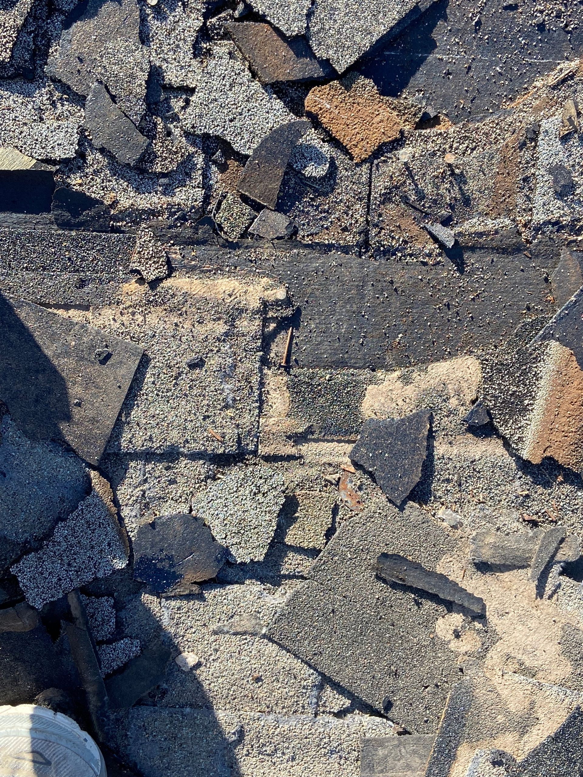 Damaged asphalt roof with scattered dark gray, brown and tan shingles.