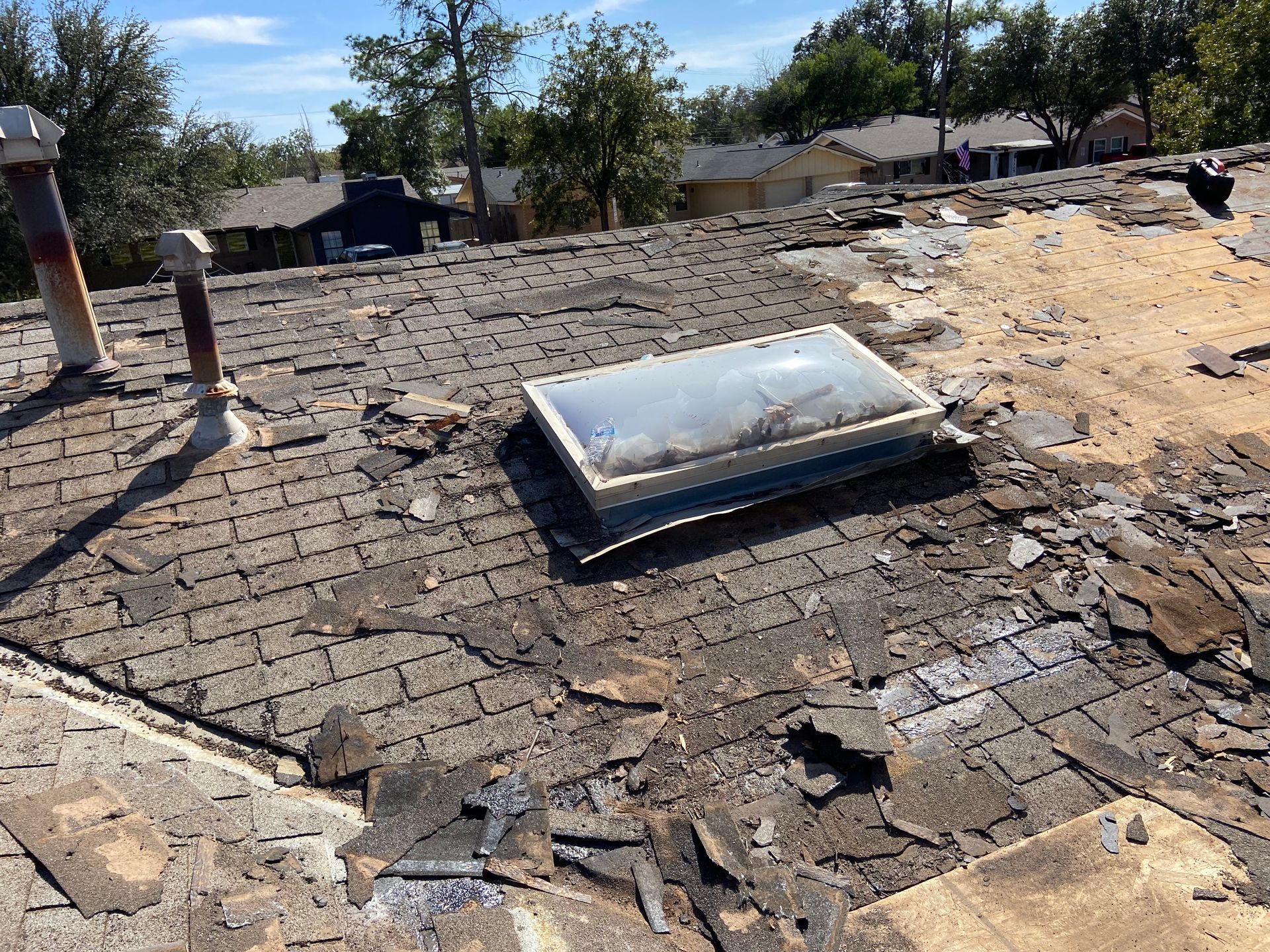 Damaged rooftop with skylight, surrounding residential neighborhood.