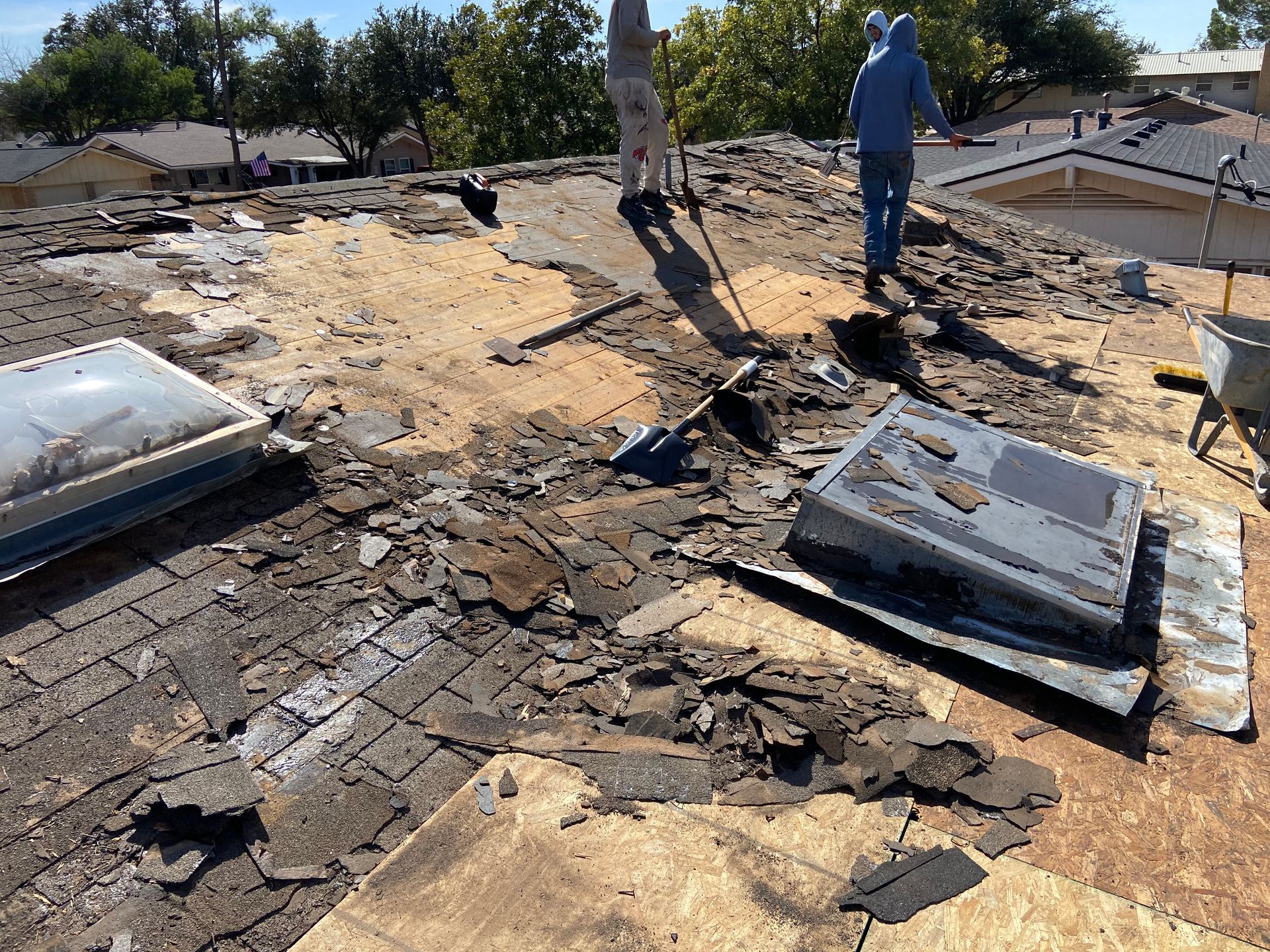 Roof being repaired; damaged shingles and debris cover the roof. A worker stands on the roof.