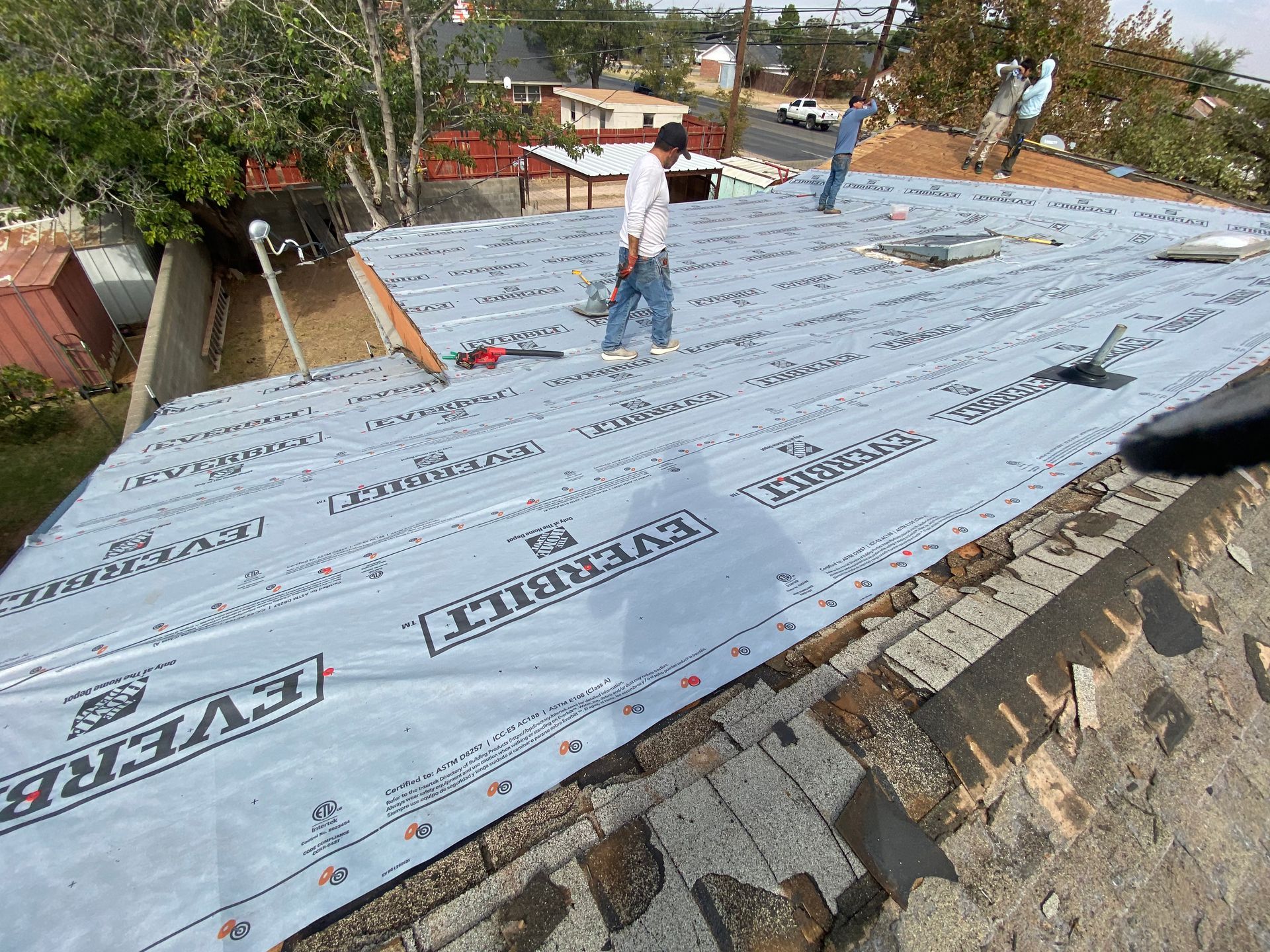 Roofing workers installing a new roof, covering the old tiles with a layer of waterproof material.