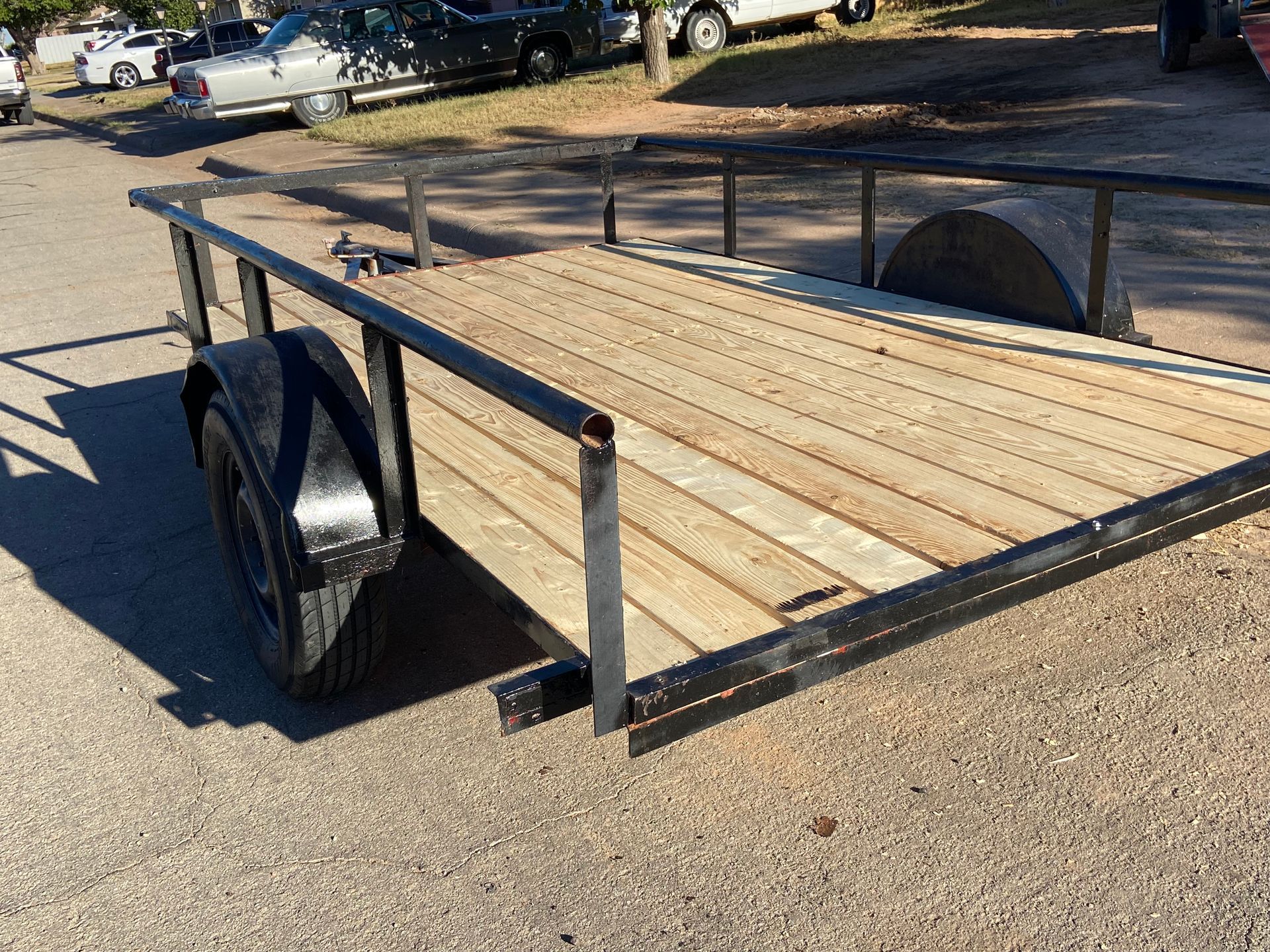 Trailer with wooden bed and black metal frame parked on asphalt.