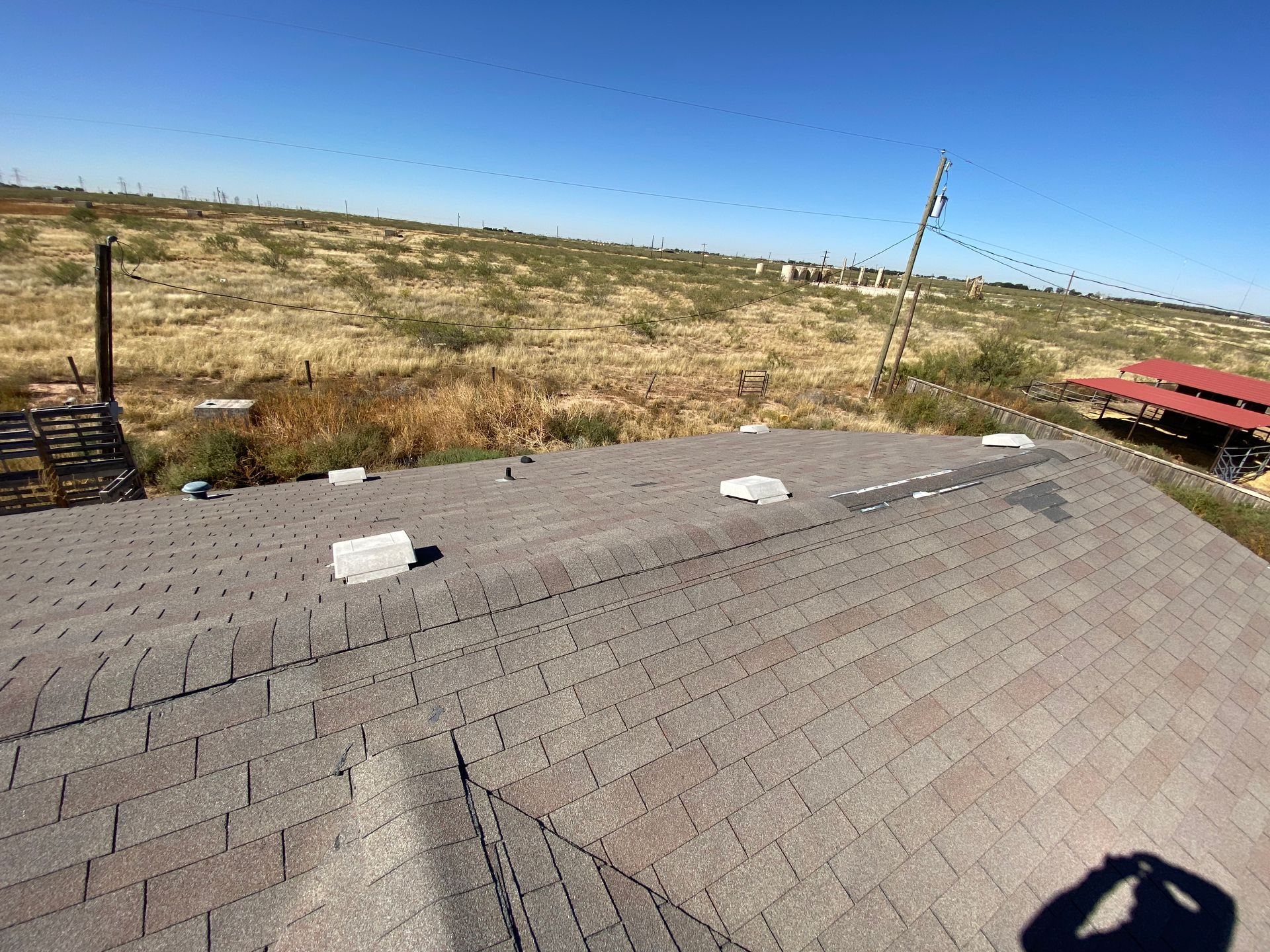 Brown shingled roof with vents, overlooking a dry, grassy landscape under a clear blue sky.