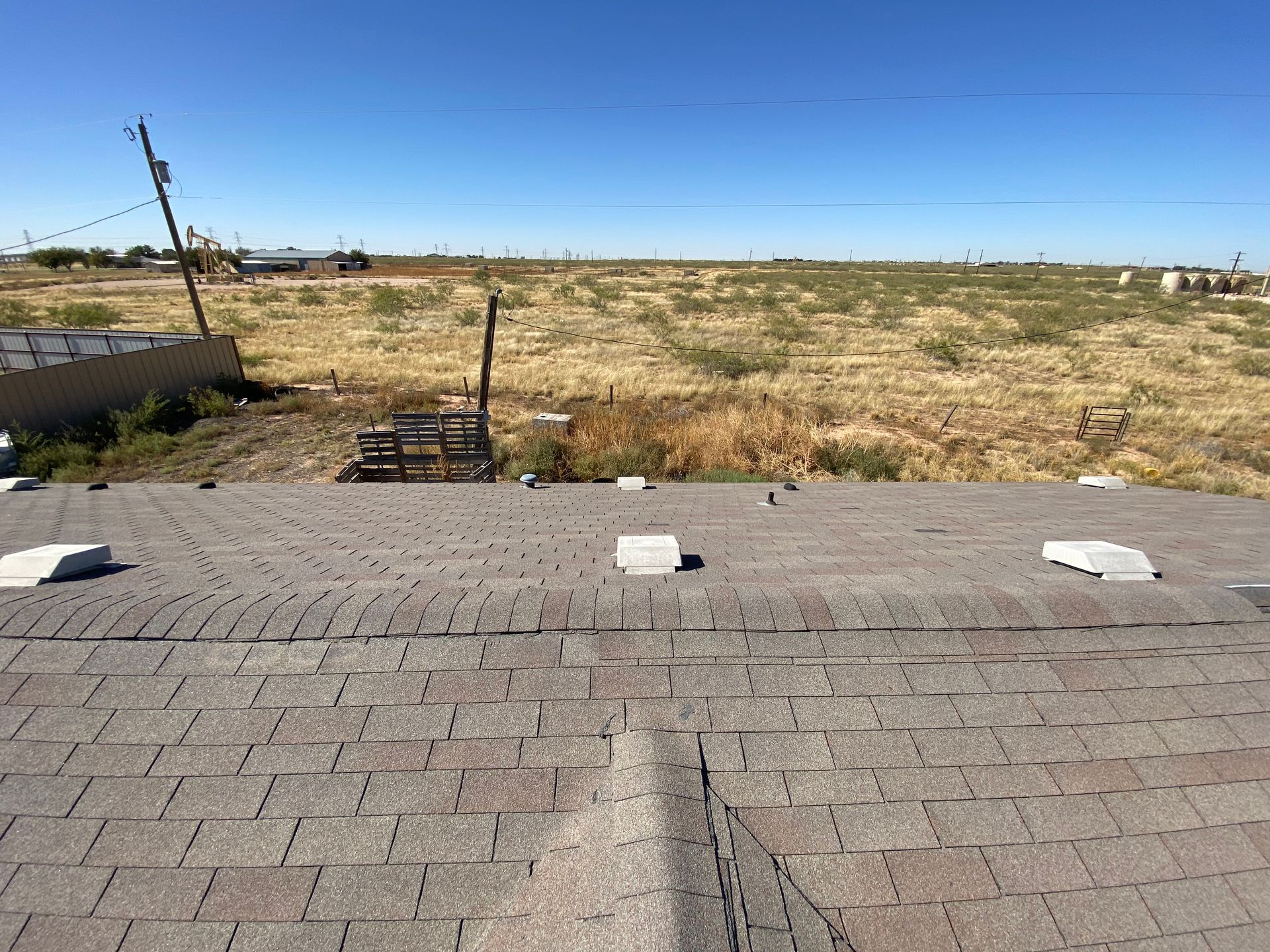 A brown shingle roof with vents in front of a field and clear sky.
