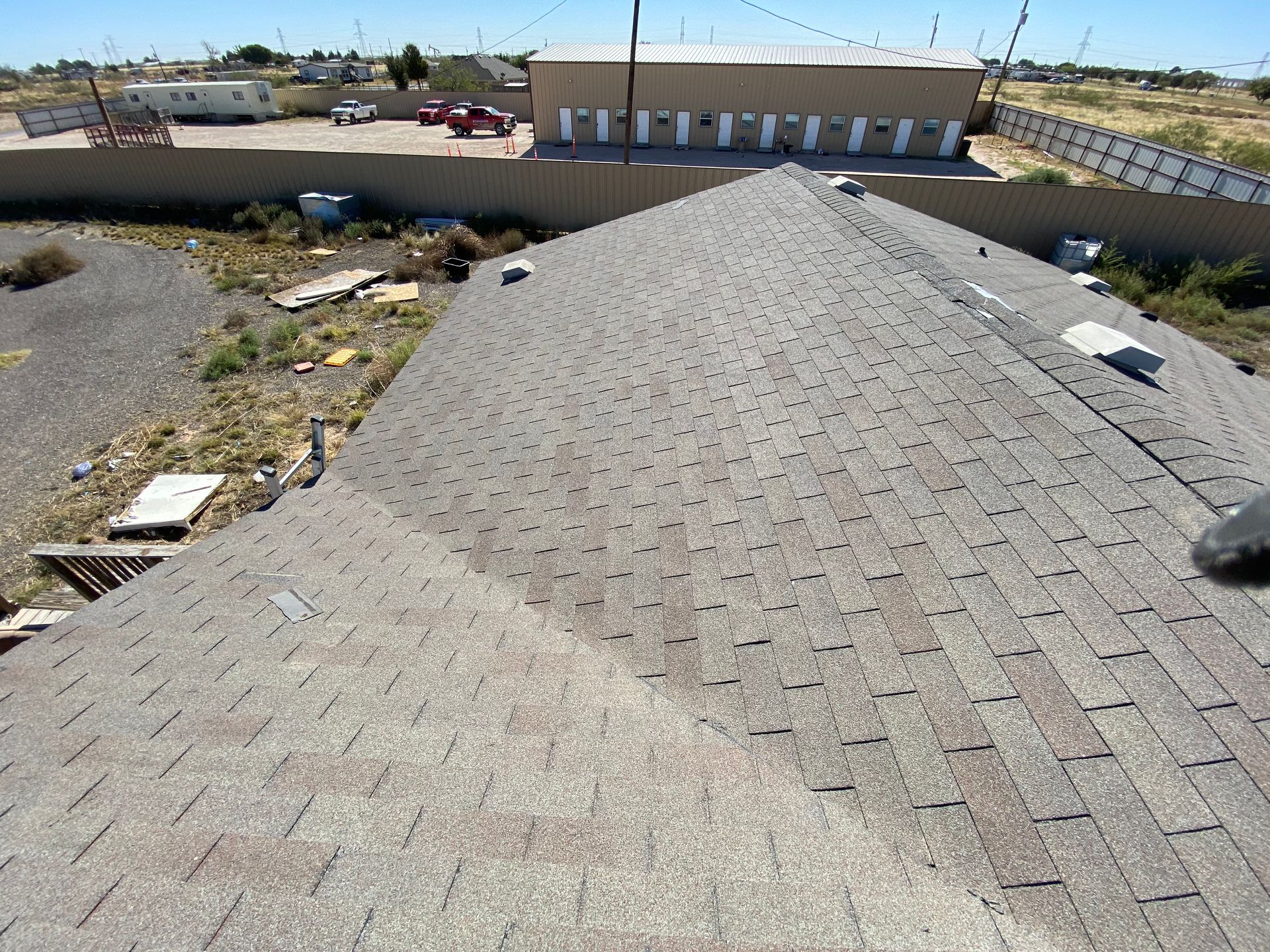 Overhead view of a shingled roof with a building and surrounding yard in the background.