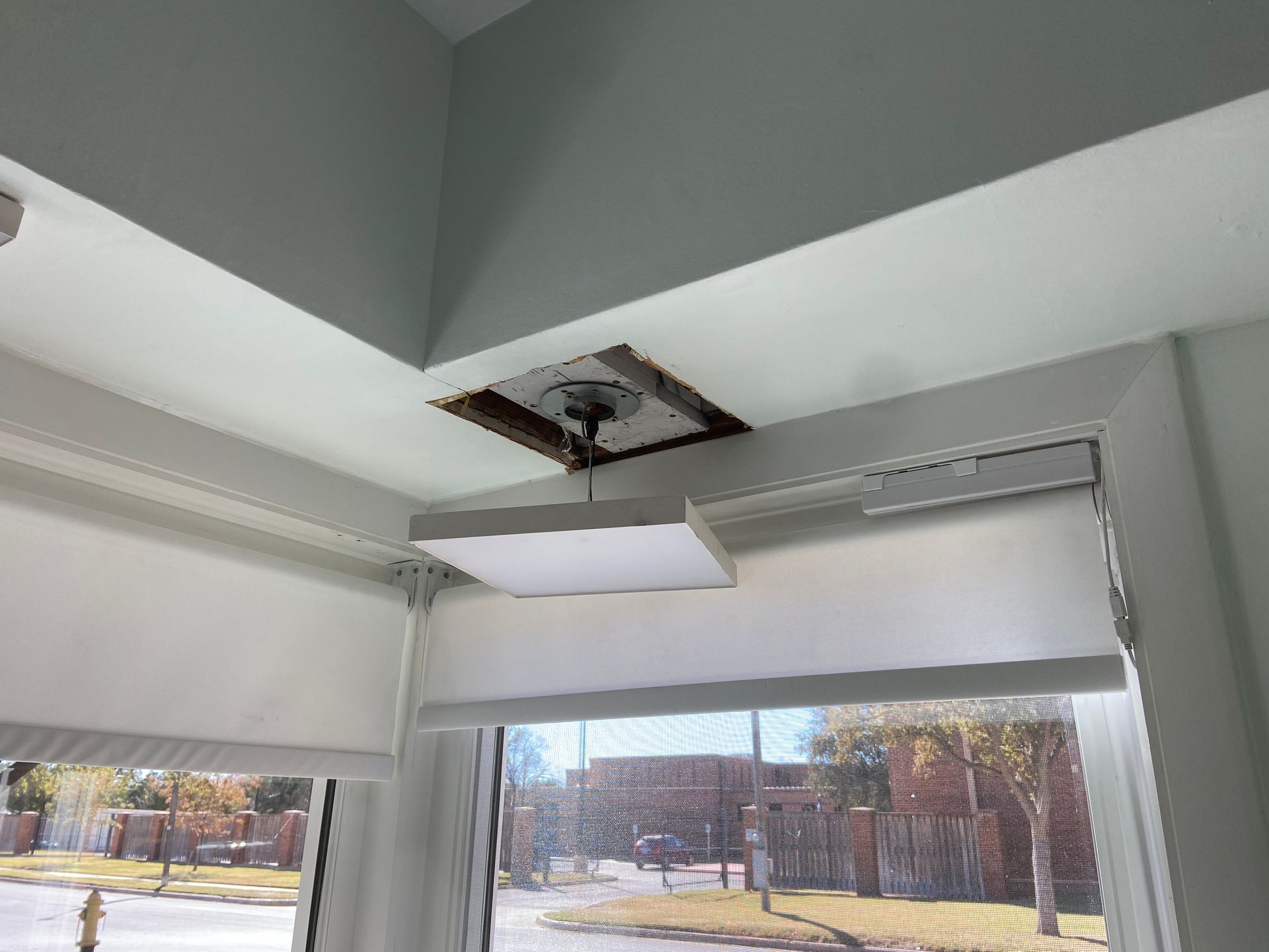 Ceiling fan electrical box exposed in a room corner, above window with blinds.