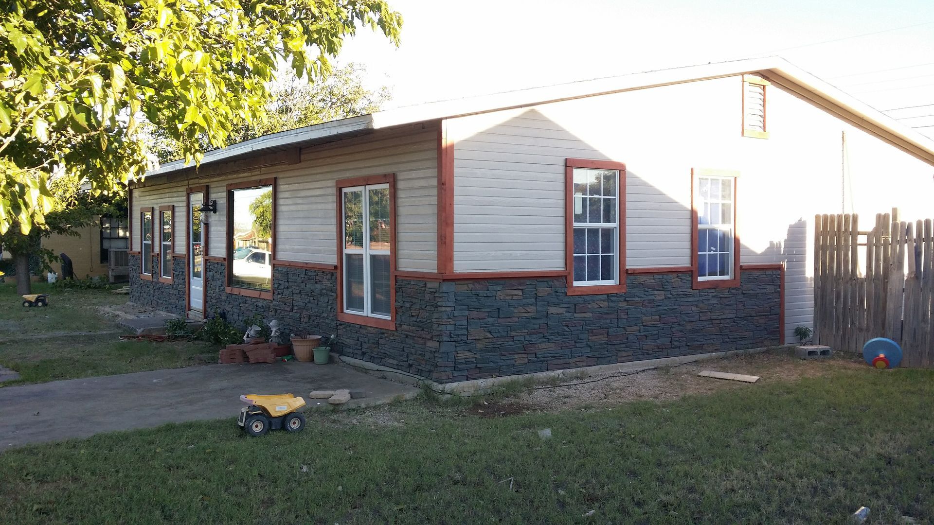 House with gray stone veneer and light siding, surrounded by a lawn and wooden fence.