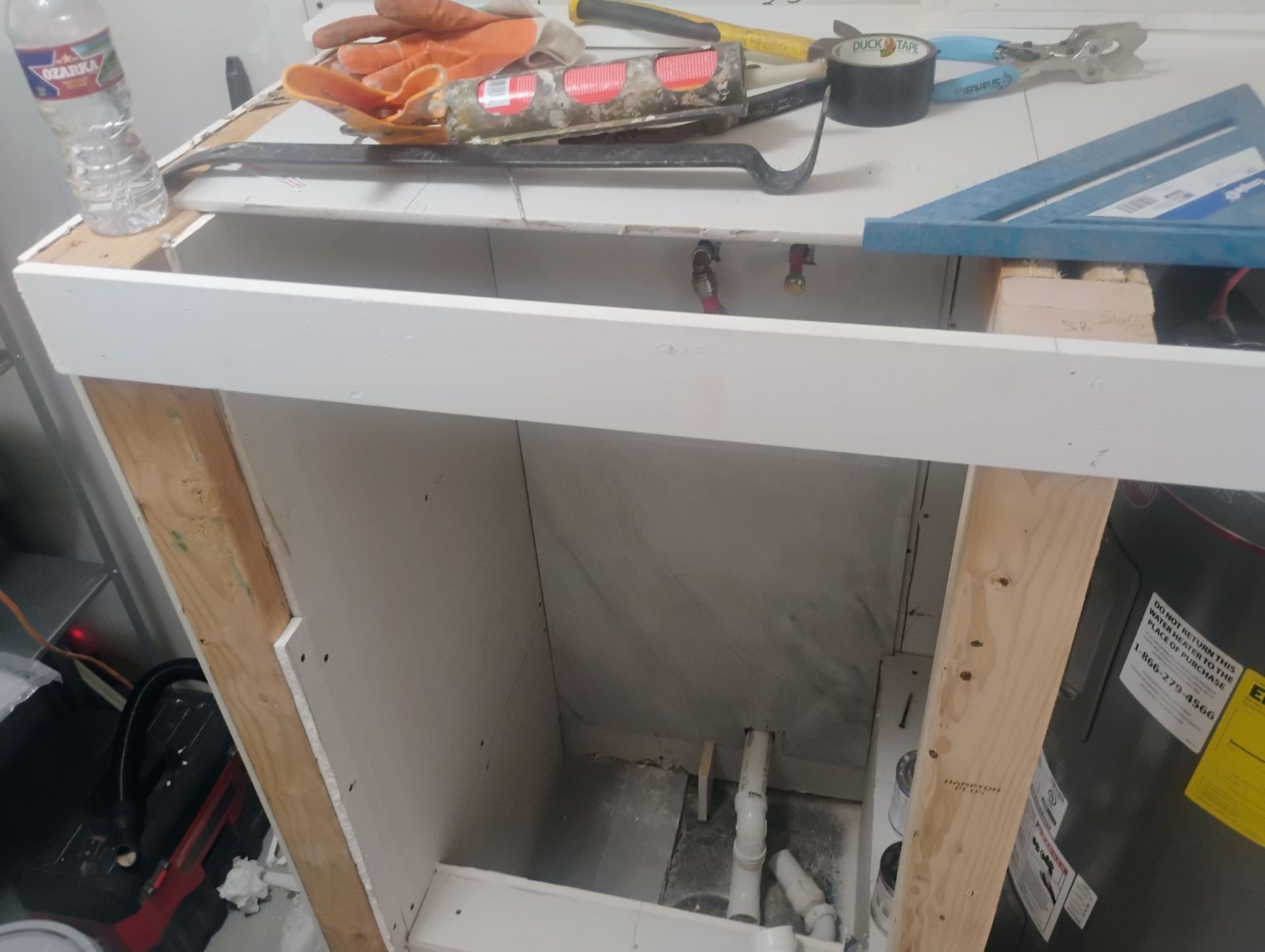 A partially constructed cabinet with tools on top, showing plumbing inside.