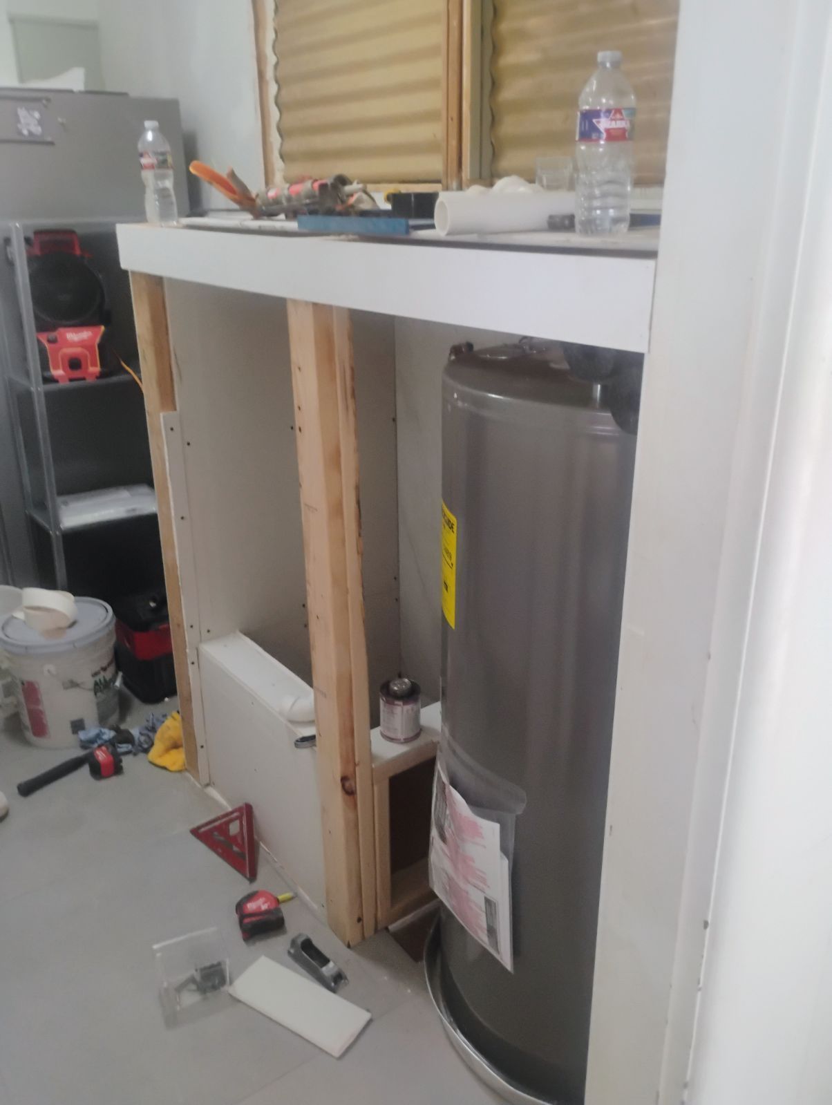 Water heater partially enclosed in a built-in cabinet during renovation. Tools and supplies scattered around.