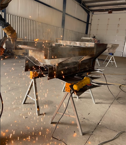 A person welds a metal structure in a shop, sparks flying.